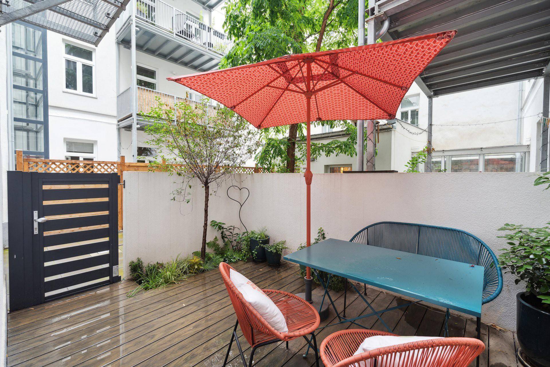 Gemütliche Terrasse mit Holzdeck, Sonnenschirm und Sitzgelegenheiten im Innenhof.