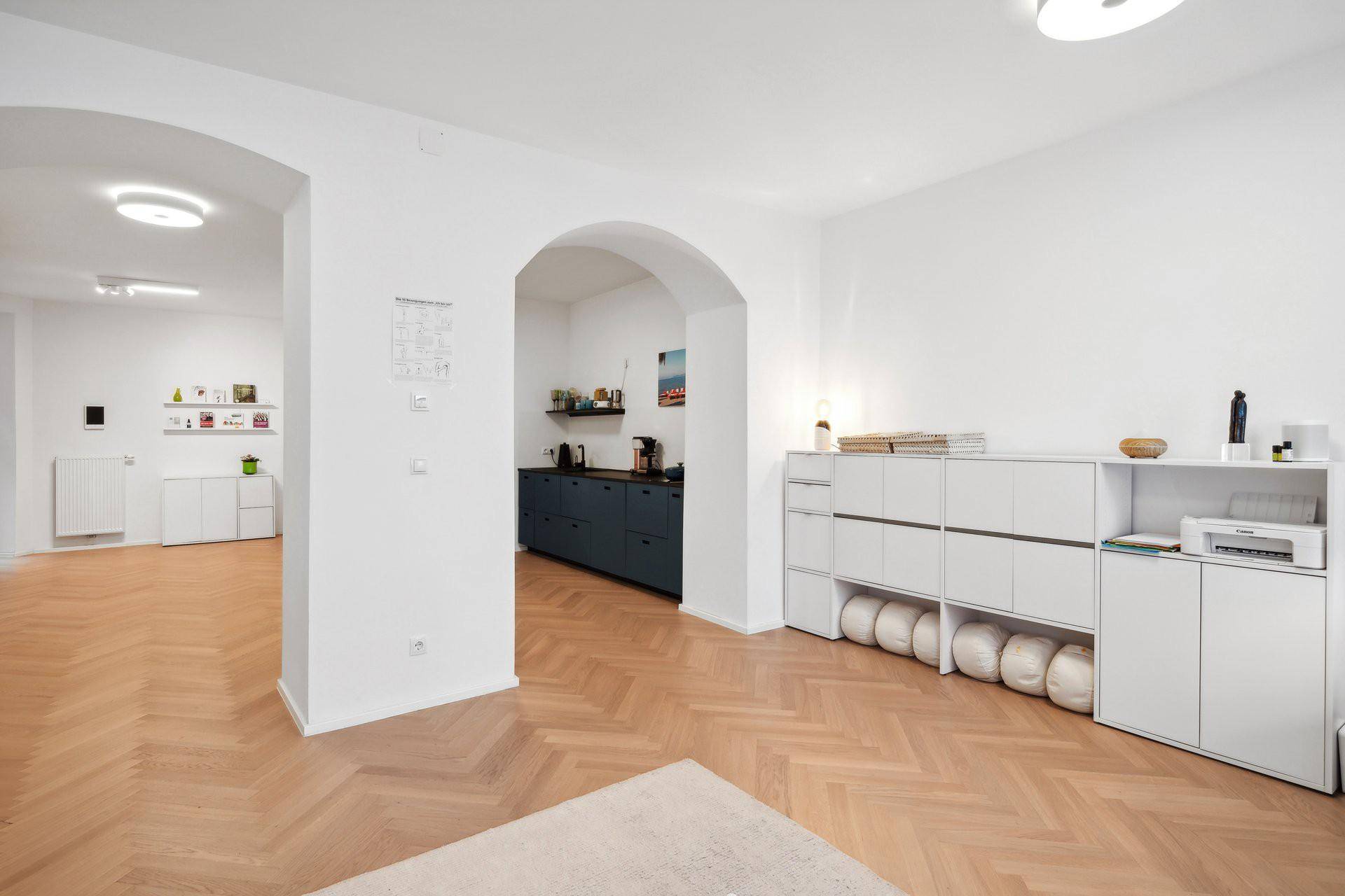 Offener Wohnbereich mit Fischgrätparkett und Blick auf die moderne Küche.