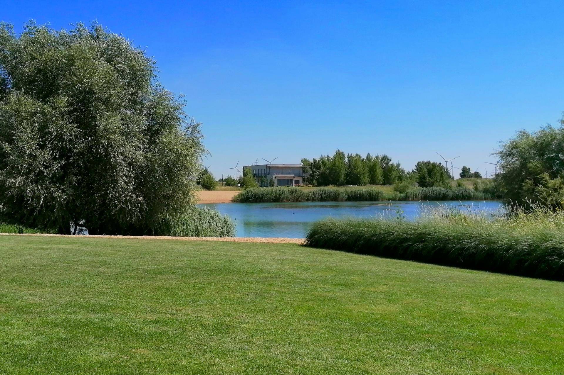 Ruhiger See mit grünen Ufern und einem modernen Gebäude in der Ferne.