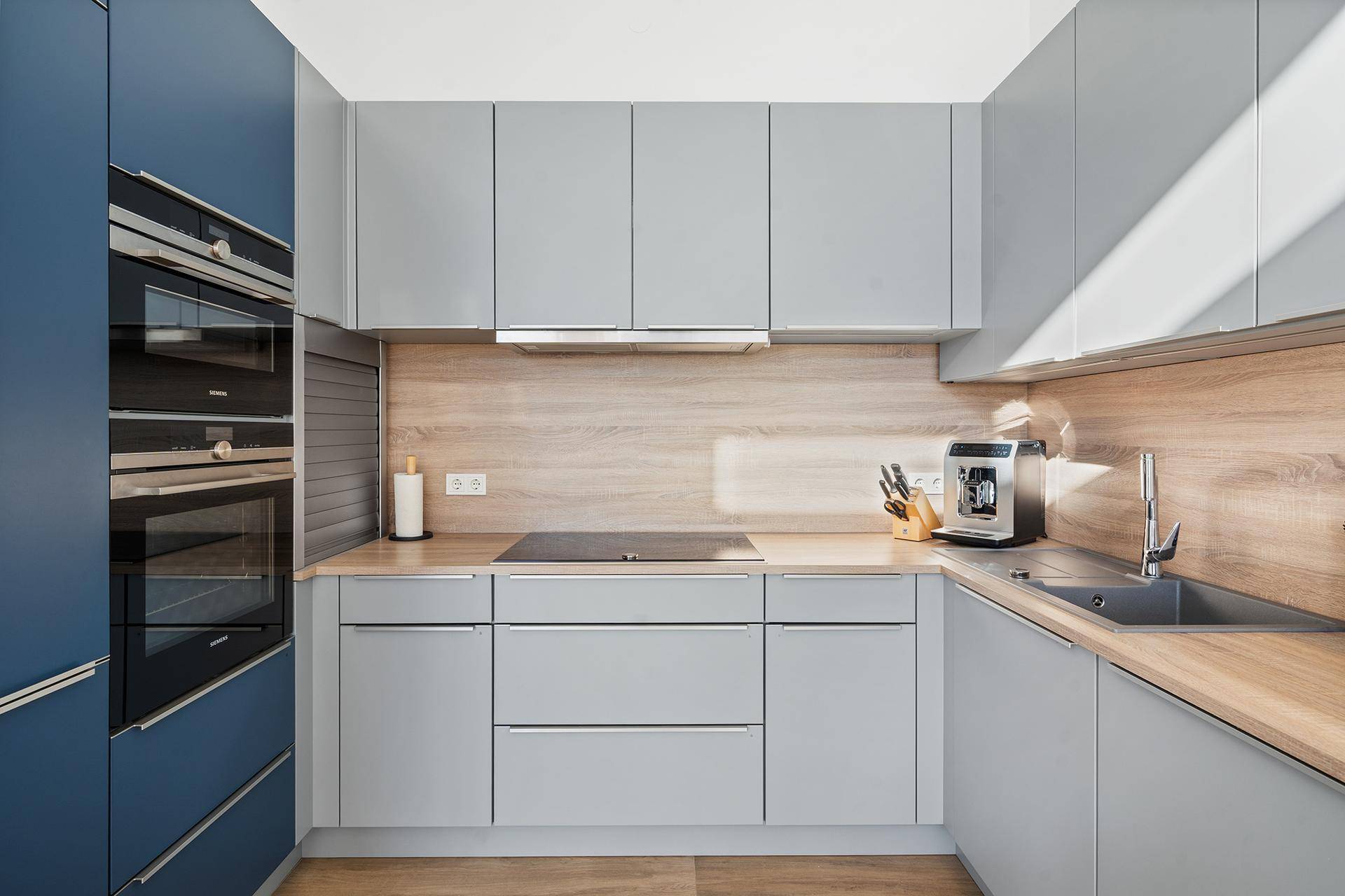 Moderne Einbauküche mit grauen Fronten, Holzdetails und hochwertigen Geräten.