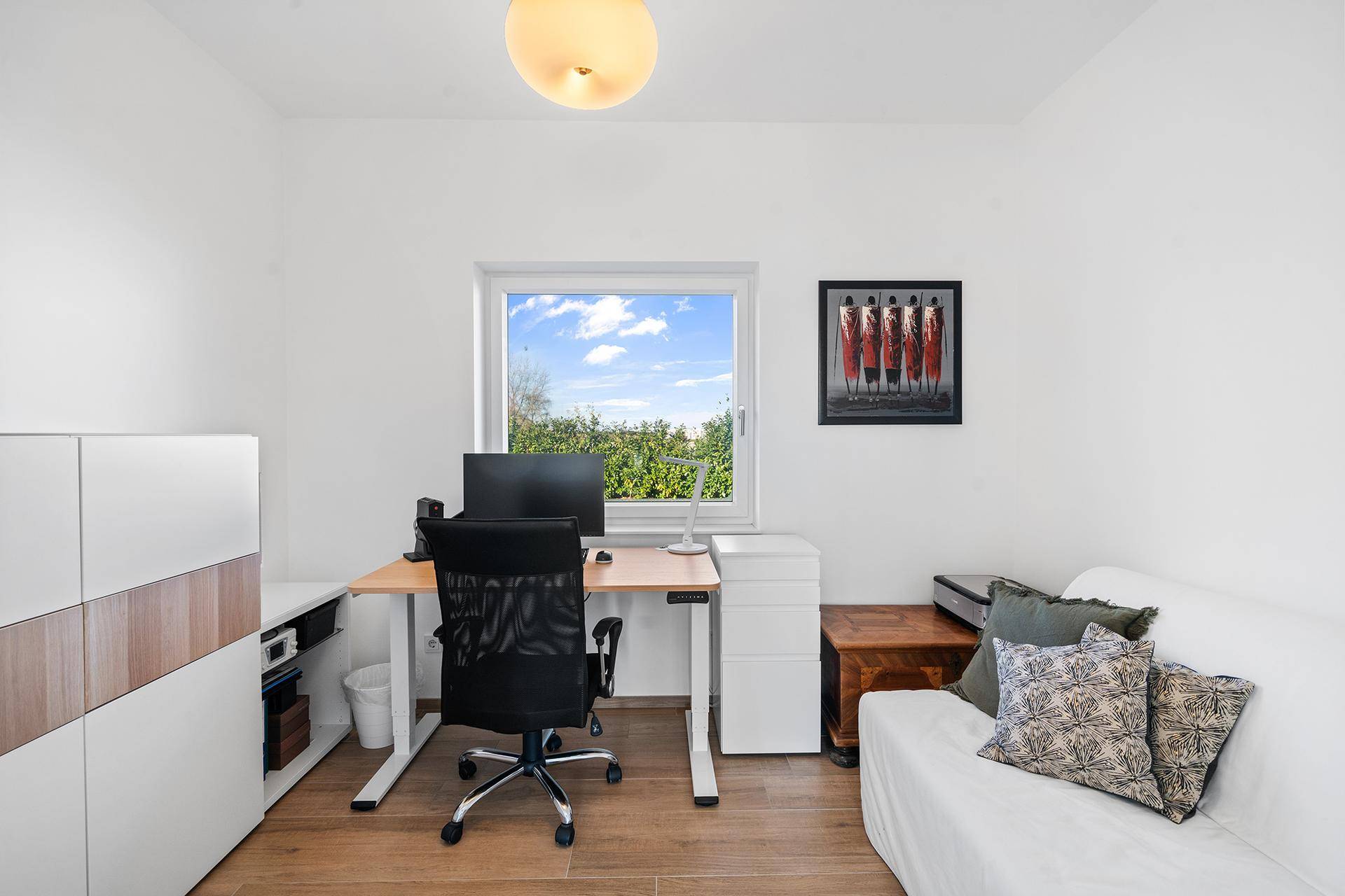 Funktionales Arbeitszimmer mit Schreibtisch, Sofa und Blick ins Grüne durch das Fenster.