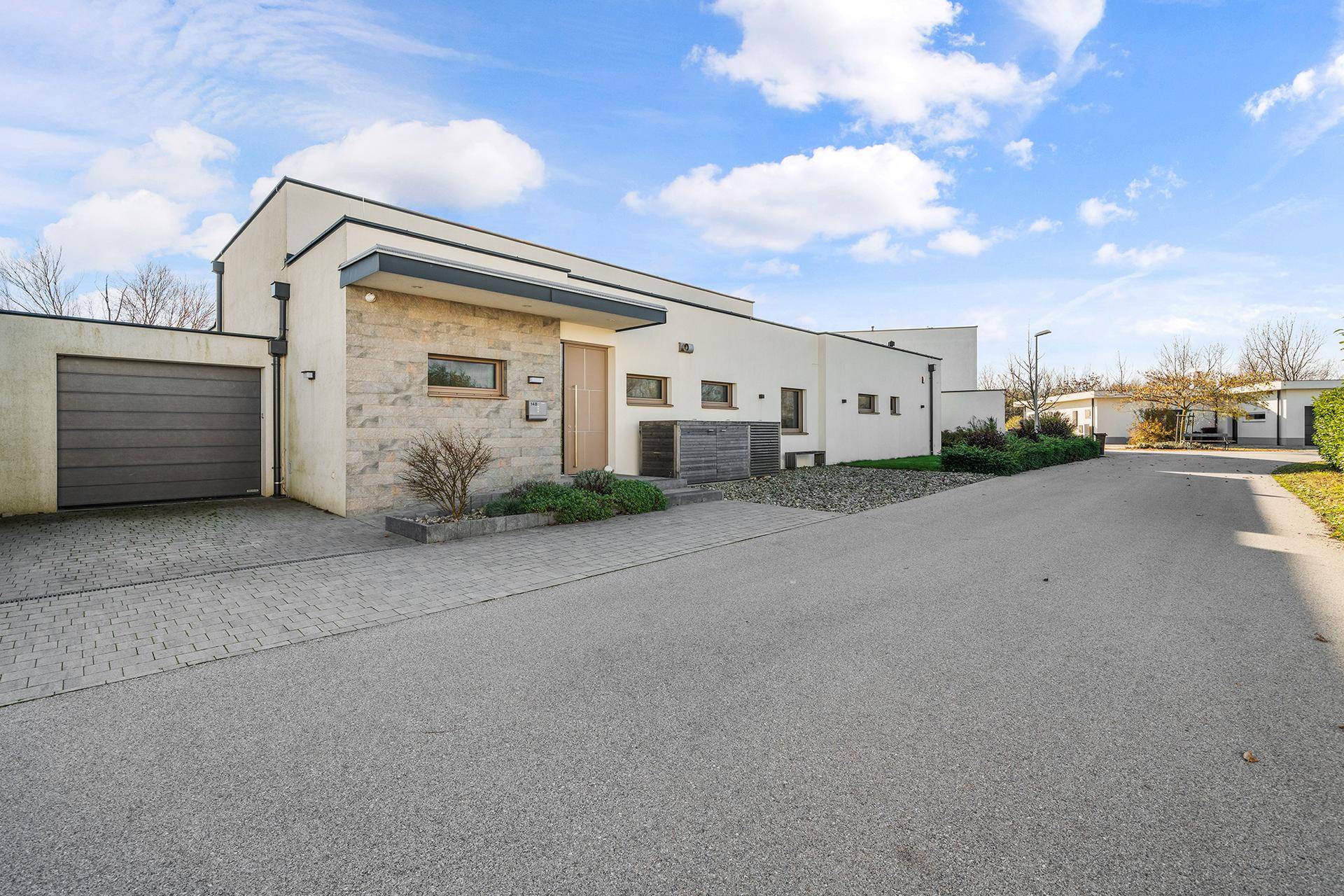 Moderne Hausfassade mit integrierter Garage und gepflasterter Auffahrt unter blauem Himmel.