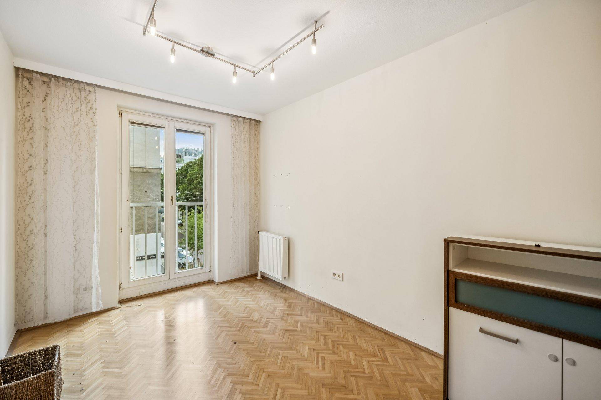 Helles Zimmer mit Fischgrätparkett und Fenster mit Blick auf die Umgebung.