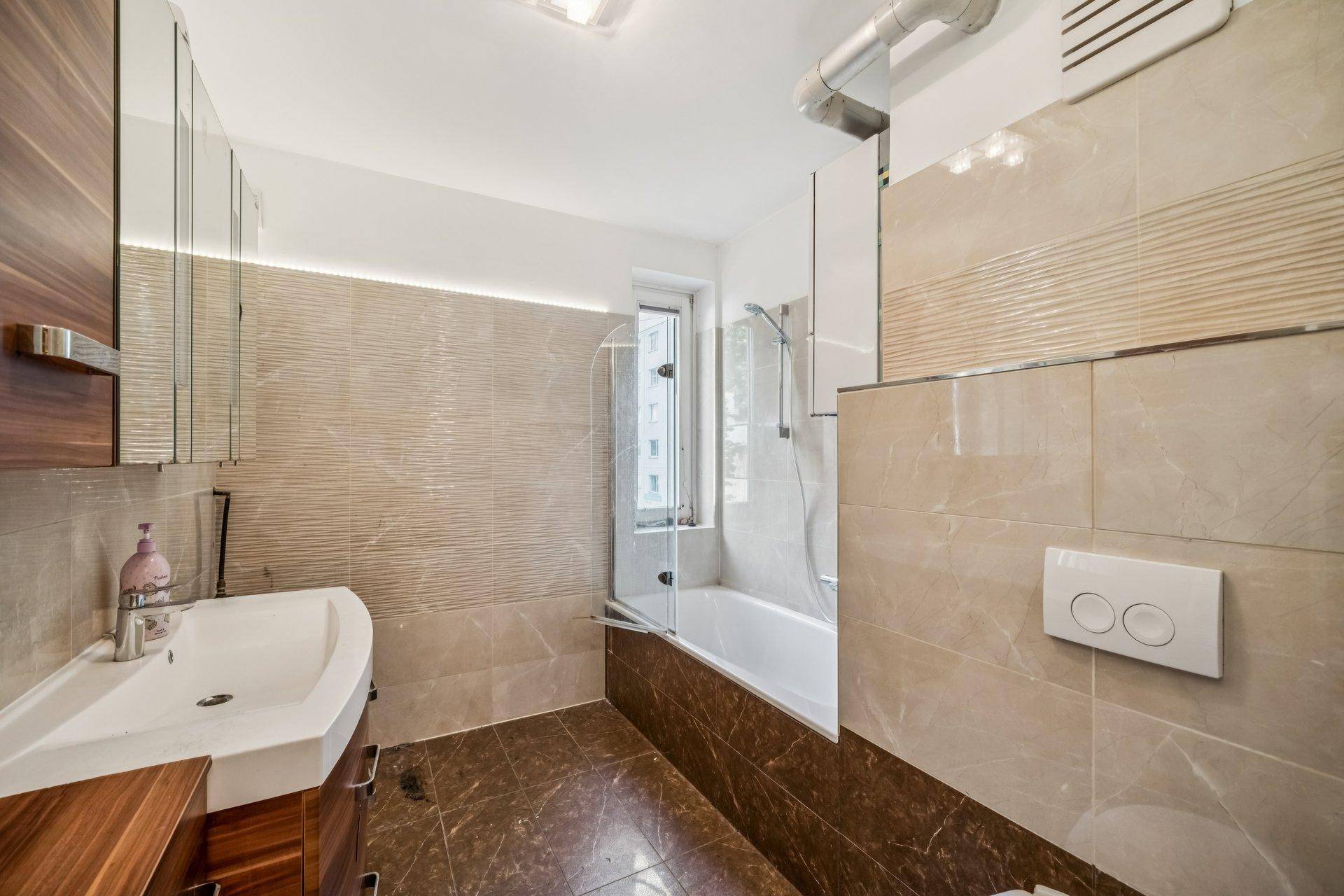 Modernes Badezimmer mit beigefarbenen Fliesen, Badewanne mit Duschwand und Einzelwaschbecken.
