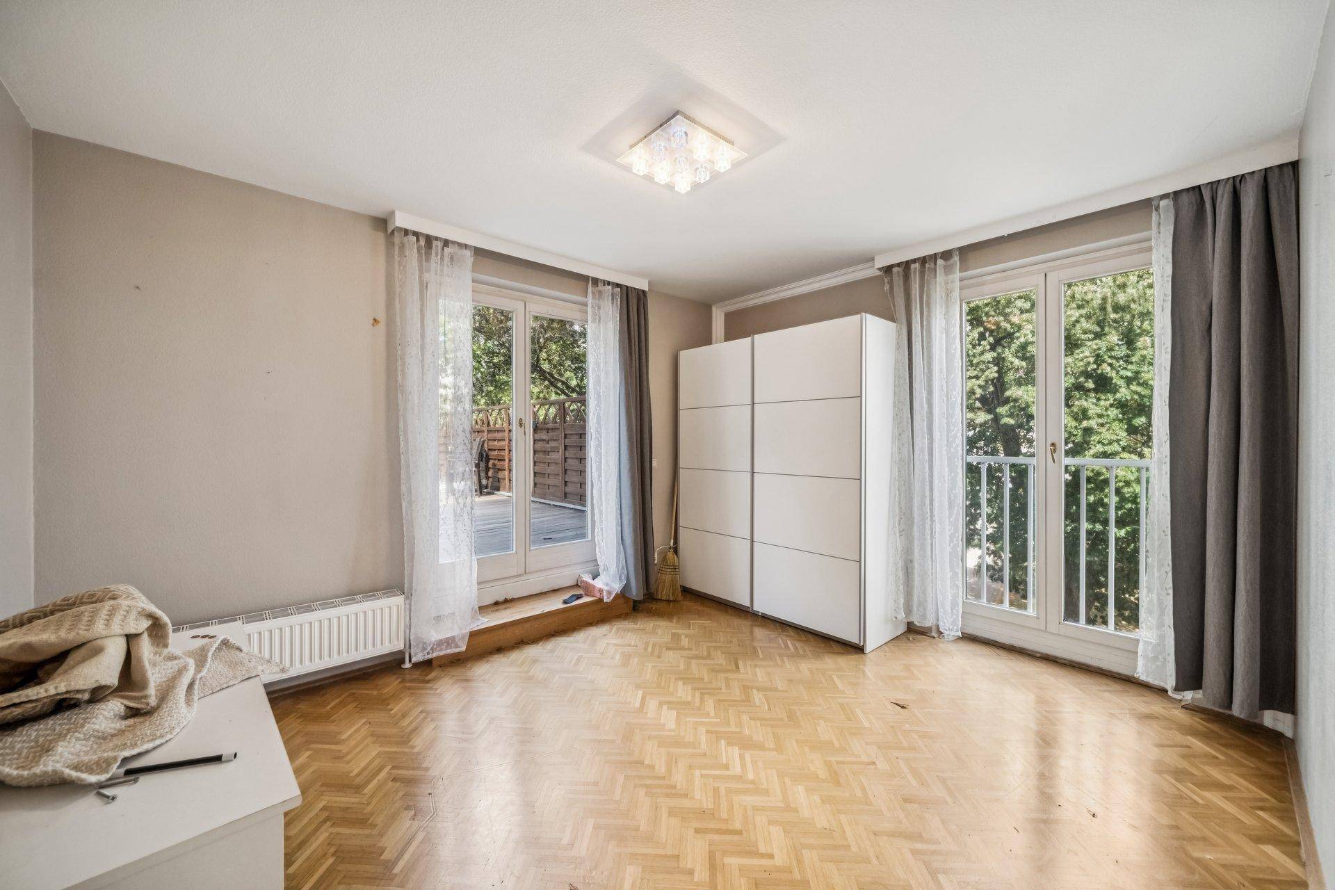 Helles Schlafzimmer mit Fischgrätparkett, großem Fenster und Zugang zu einem französischen Balkon.