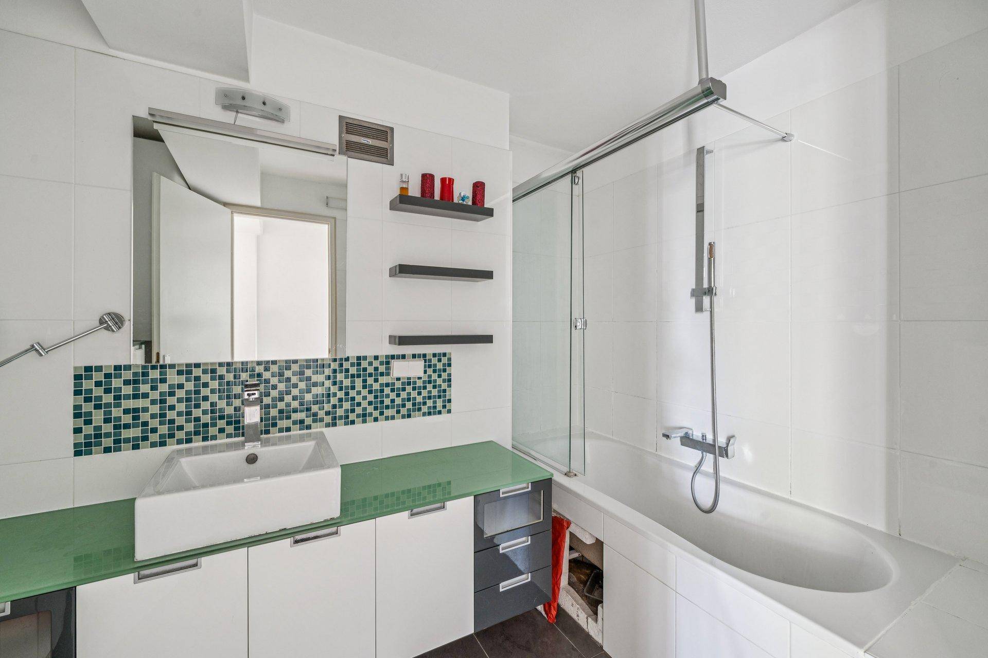 Modernes Badezimmer mit Badewanne, Dusche und einem Waschbecken mit grüner Ablagefläche.