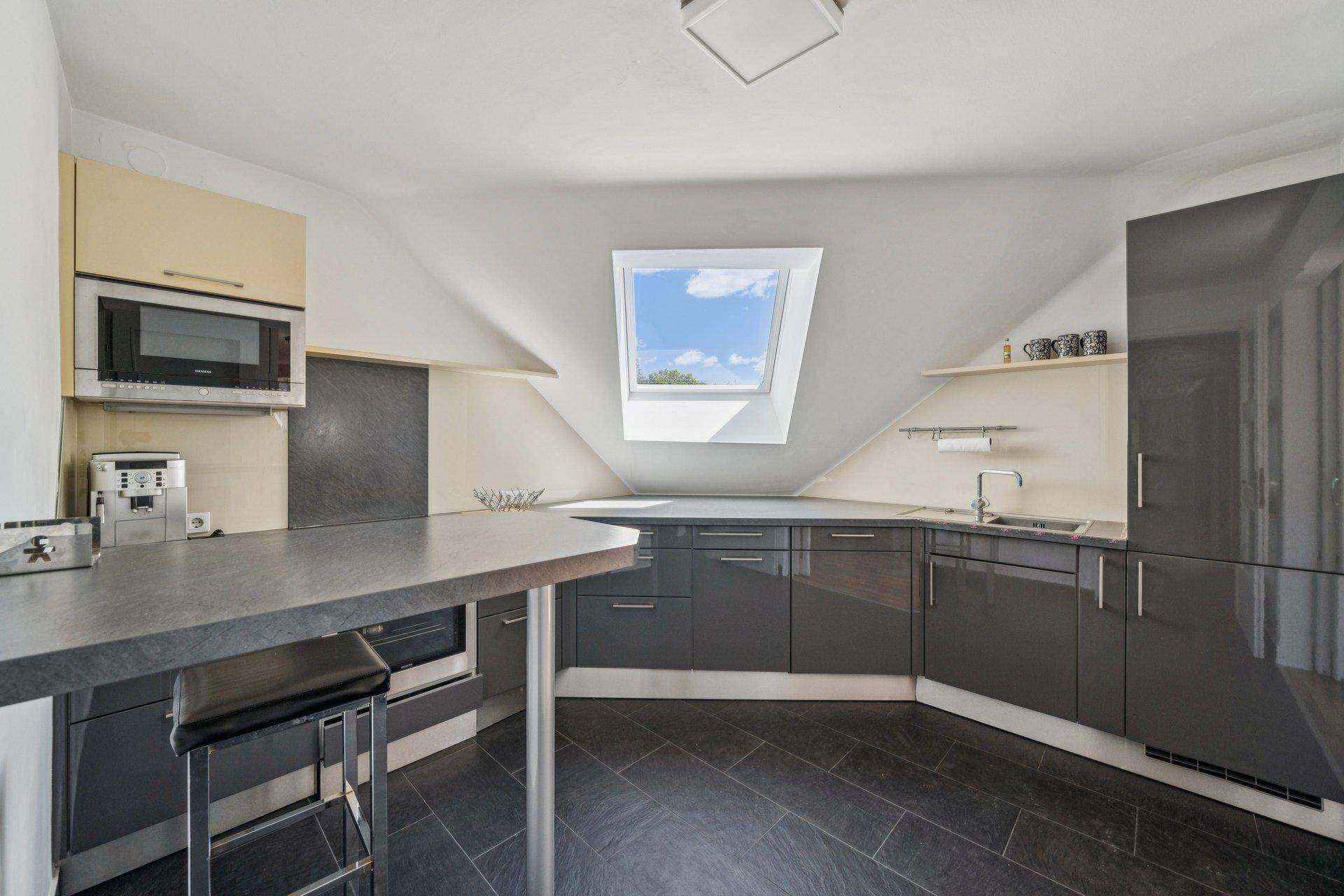 Moderne Küche mit grauen Hochglanzfronten, Dachfenster und integrierten Geräten unter Dachschrägen.