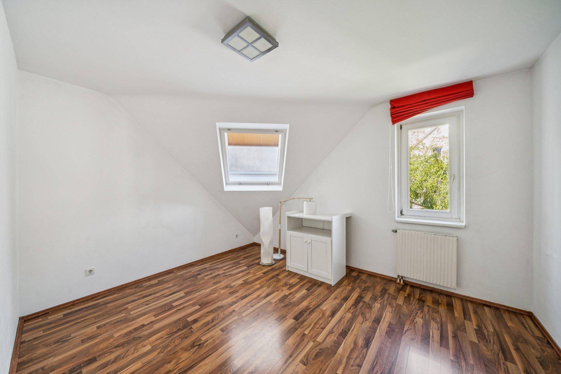 Helles Zimmer mit Holzboden, Dachfenster und Heizkörper, ideal als Schlaf- oder Arbeitszimmer.