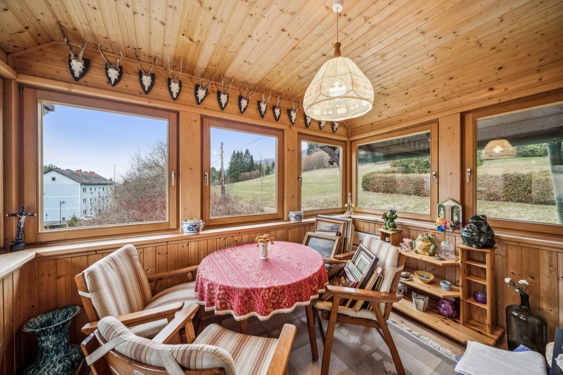 Gemütlicher Wintergarten mit Holzverkleidung, Sitzgelegenheiten und Blick auf die Natur.