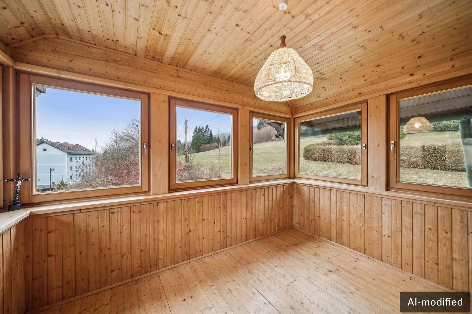 Heller Wintergarten mit Holzverkleidung, großen Fenstern und Blick auf die grüne Landschaft.