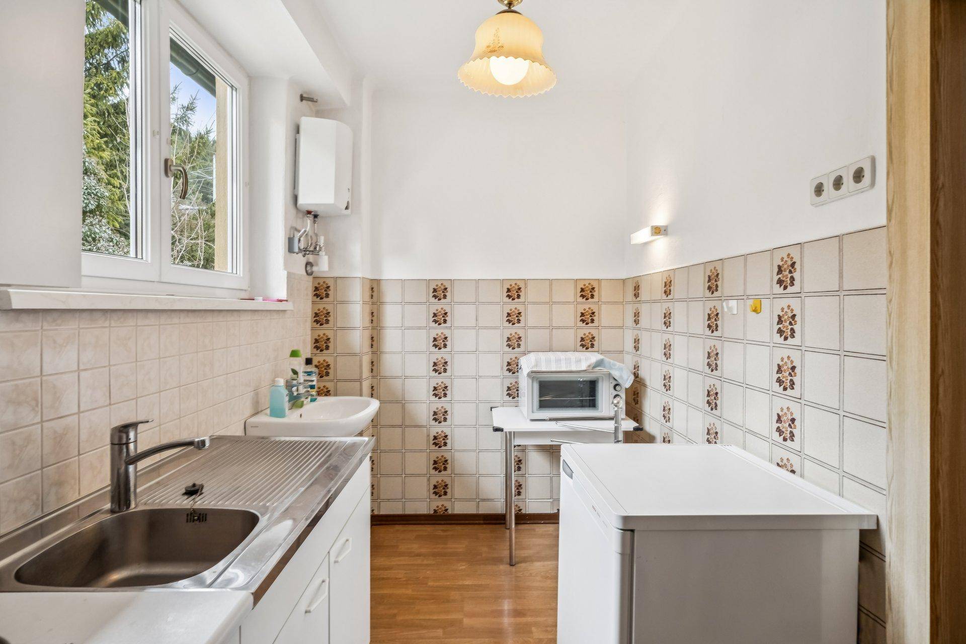 Funktionale Küche mit Spülbecken, Mikrowelle und traditionellen Fliesen an der Wand.