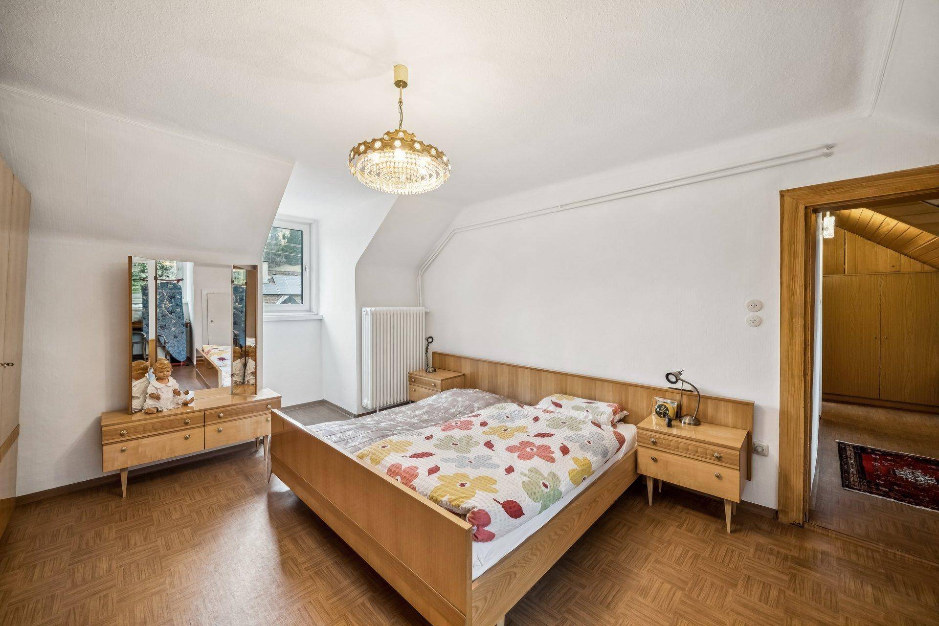 Helles Schlafzimmer im Dachgeschoss mit Holzfußboden, modernem Bett und Kommode.