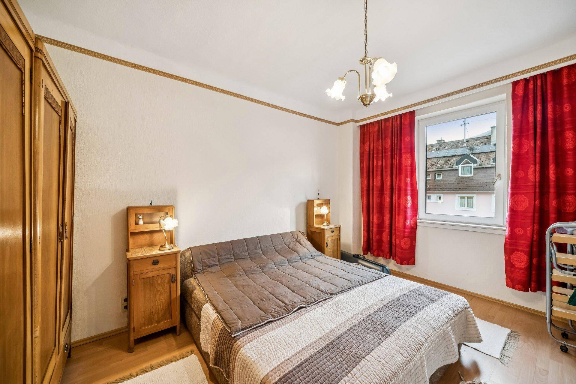 Schlafzimmer mit traditionellen Holzmöbeln, rotem Vorhang und einem Doppelbett.