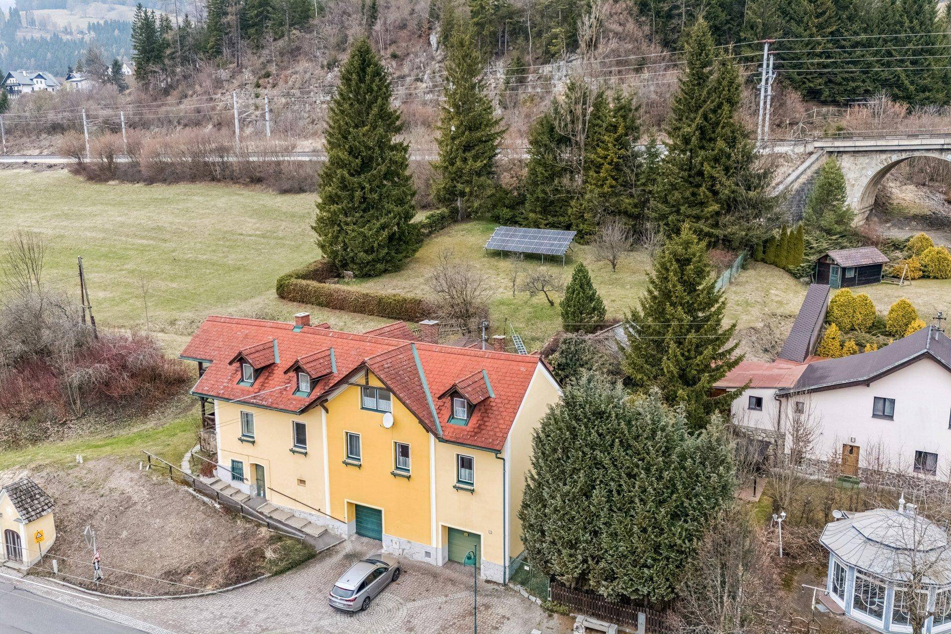 Traditionelles Haus mit rotem Ziegeldach, umgeben von grüner Landschaft und Bergen.