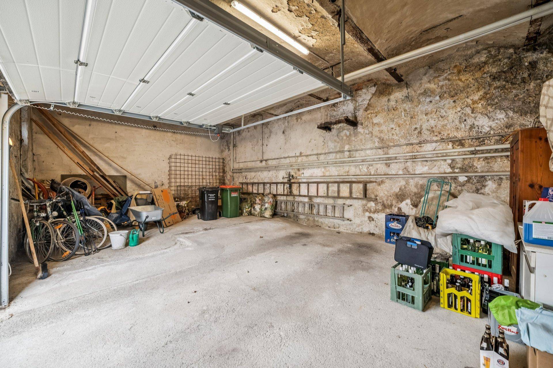 Geräumige Garage mit Betonboden und Lagerfläche für Fahrräder und Kisten.