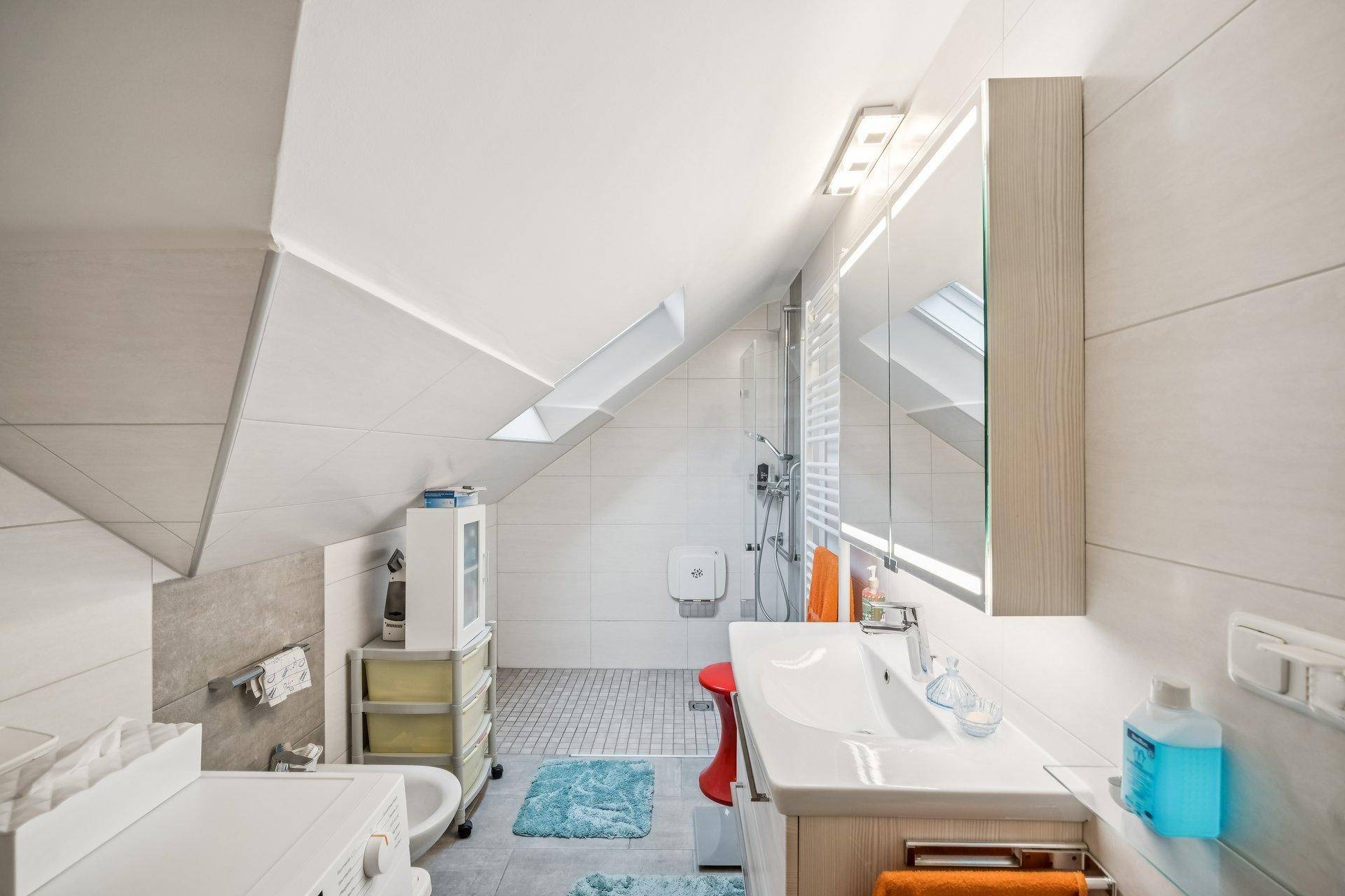 Modernes Badezimmer im Dachgeschoss mit Dusche, Waschbecken und Dachfenster.