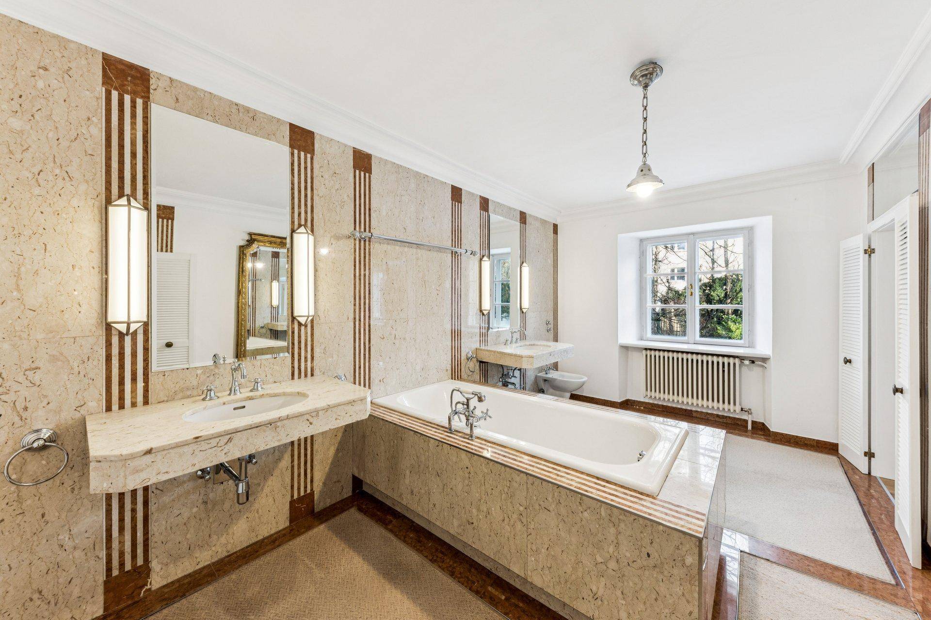 Geräumiges Badezimmer mit eleganten Marmorfliesen, Doppelwaschbecken und einer eingebauten Badewanne.