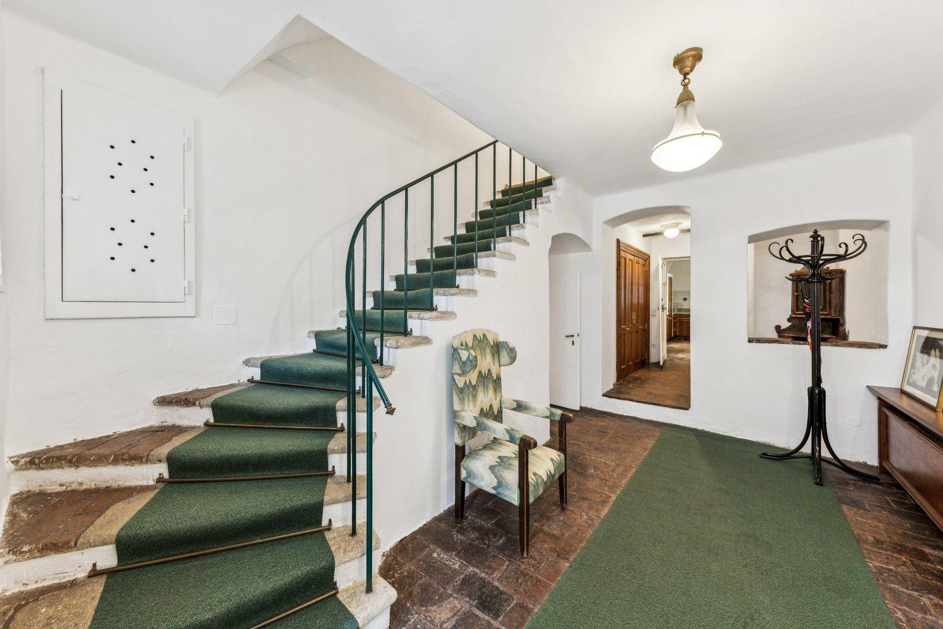 Historischer Flur mit geschwungener Treppe, grünem Teppich und traditioneller Einrichtung.