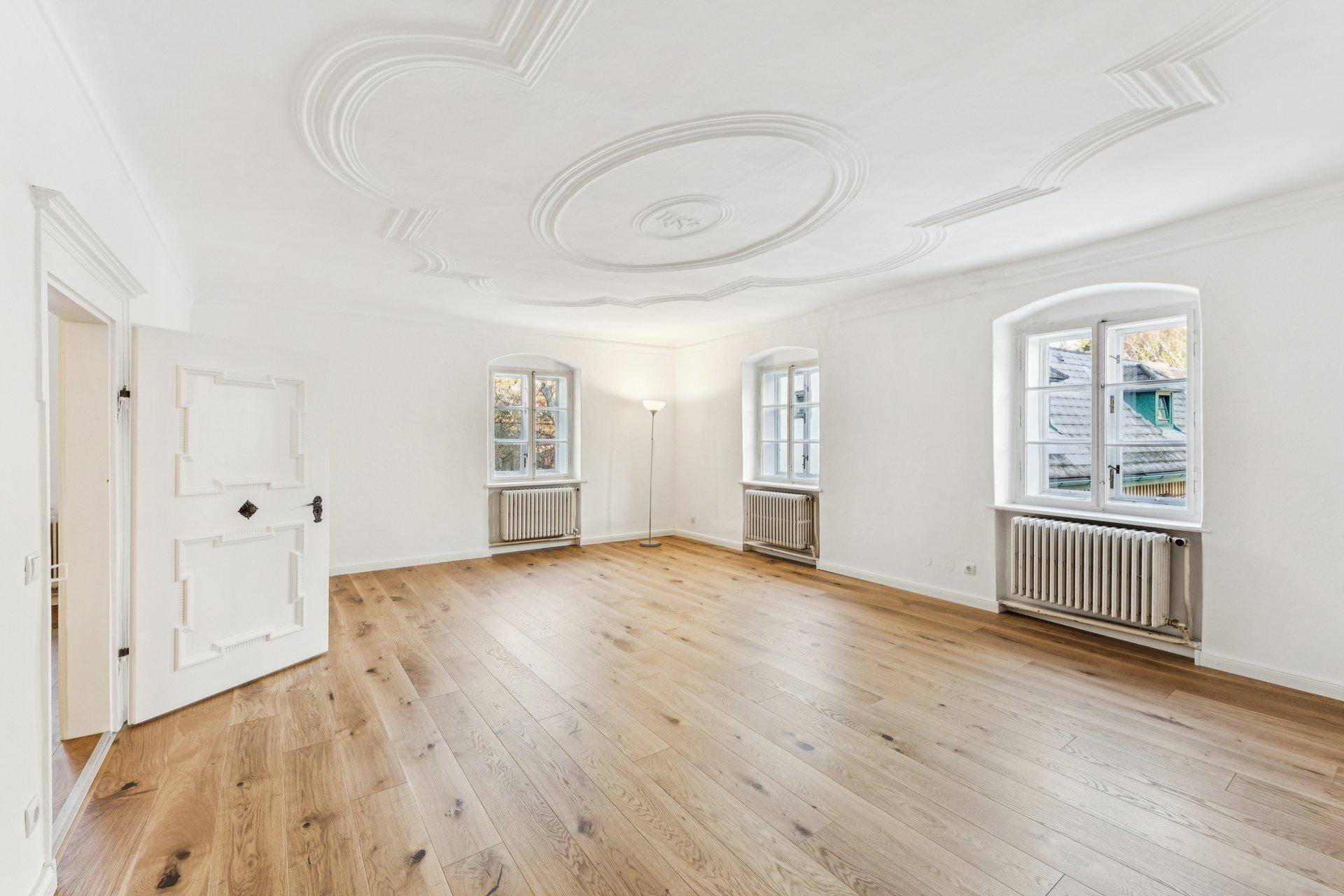 Helles Wohnzimmer mit elegantem Stuck an der Decke, breiten Holzdielen und großen Fenstern.