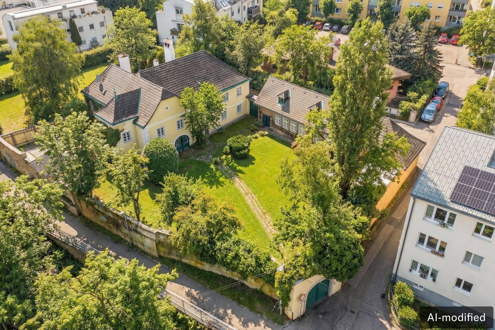 Luftaufnahme des Anwesens mit dem historischen Gebäude, weitläufigen Grünflächen und umliegenden Häusern.