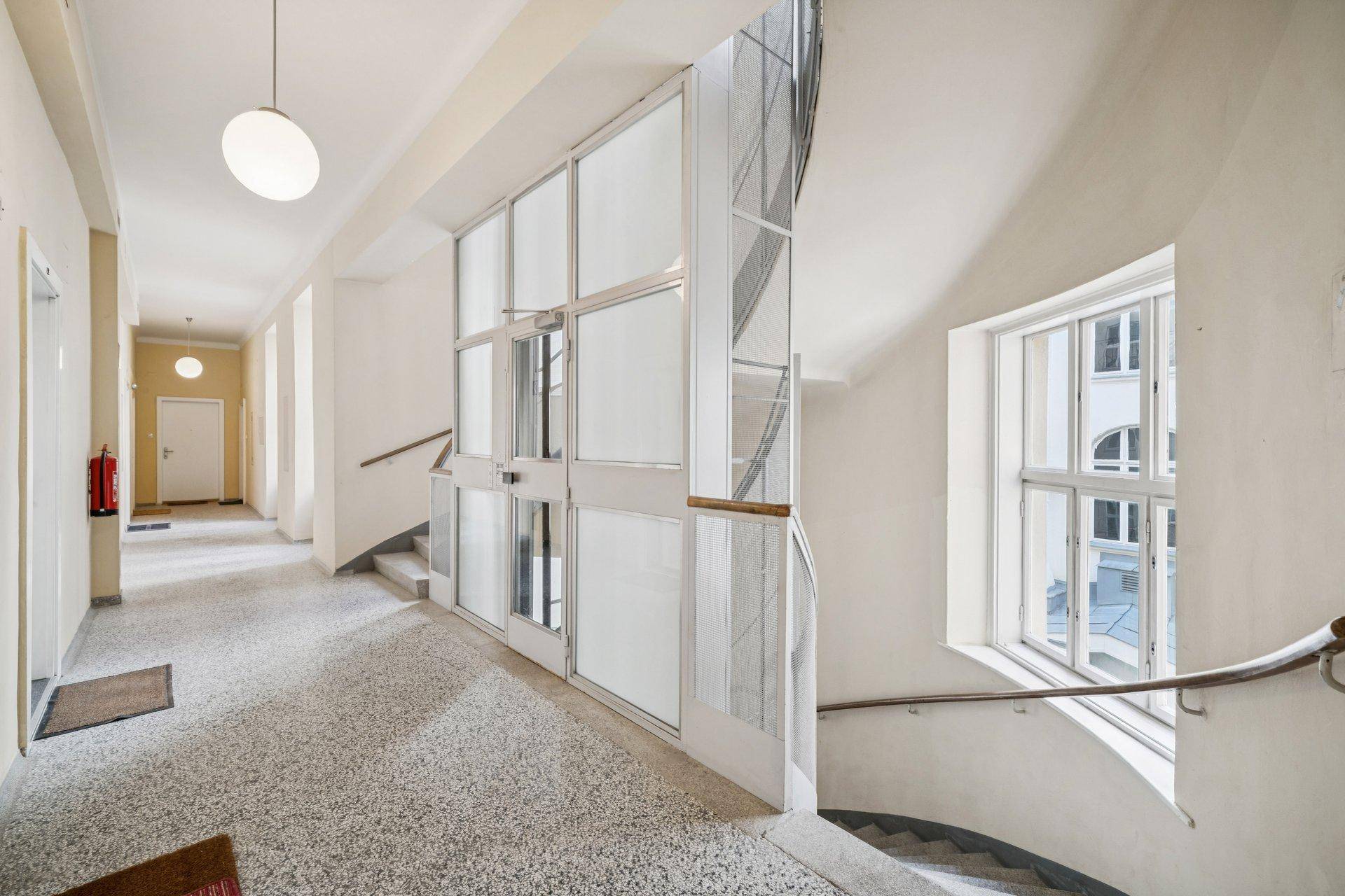 Heller Flur mit Terrazzoboden, einer modernen Glasliftanlage und einer geschwungenen Treppe.