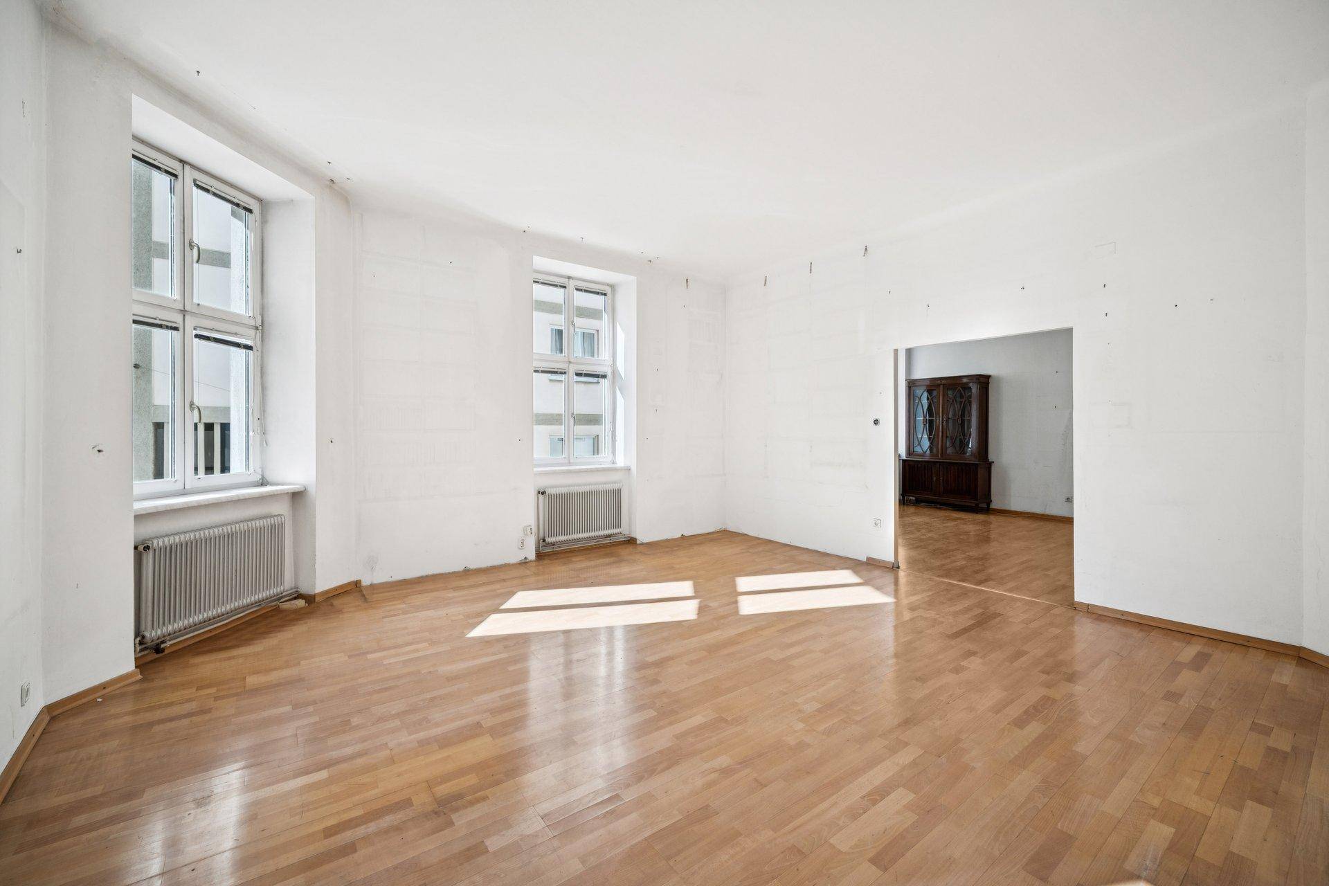 Großes, helles Zimmer mit Parkettboden und Fenstern, das viel Tageslicht empfängt.