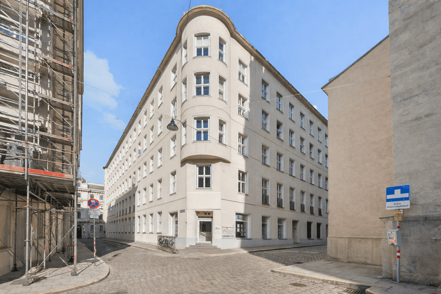Elegantes Eckgebäude mit heller Fassade und vielen Fenstern an einer gepflasterten Straße.