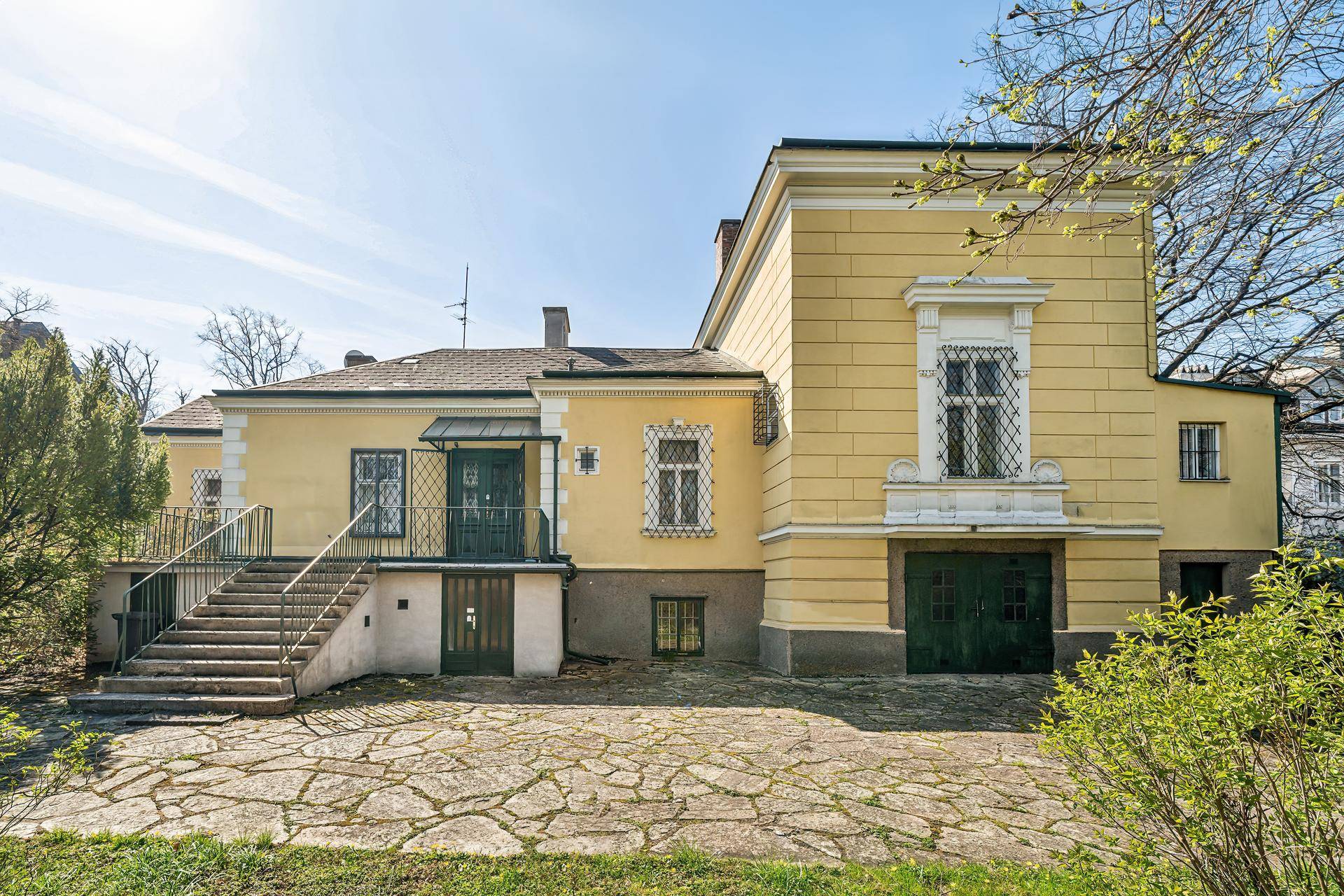 Seitenansicht des historischen Gebäudes mit Außentreppe und gepflastertem Vorplatz.