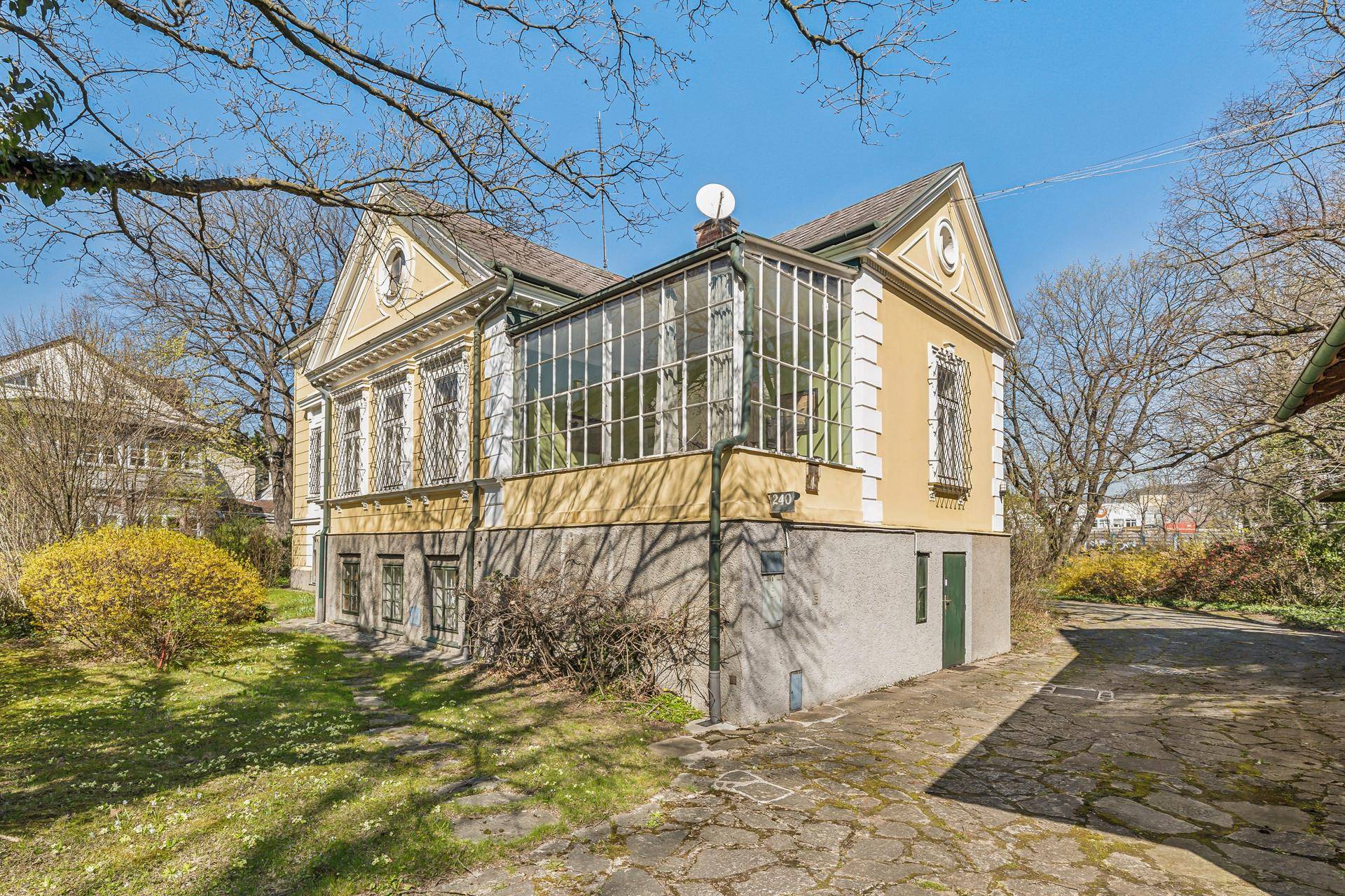 Historisches Gebäude mit verglastem Wintergarten und gepflegtem Gartenbereich.