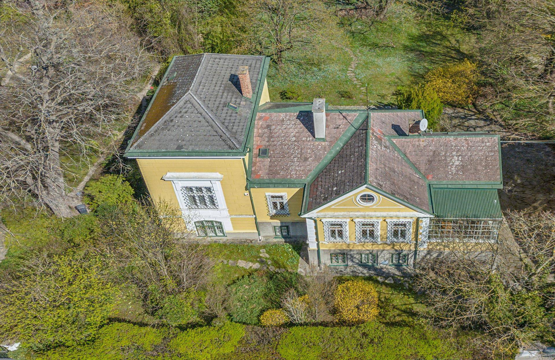 Luftaufnahme des historischen Gebäudes mit Satteldach und umgebender grüner Landschaft.