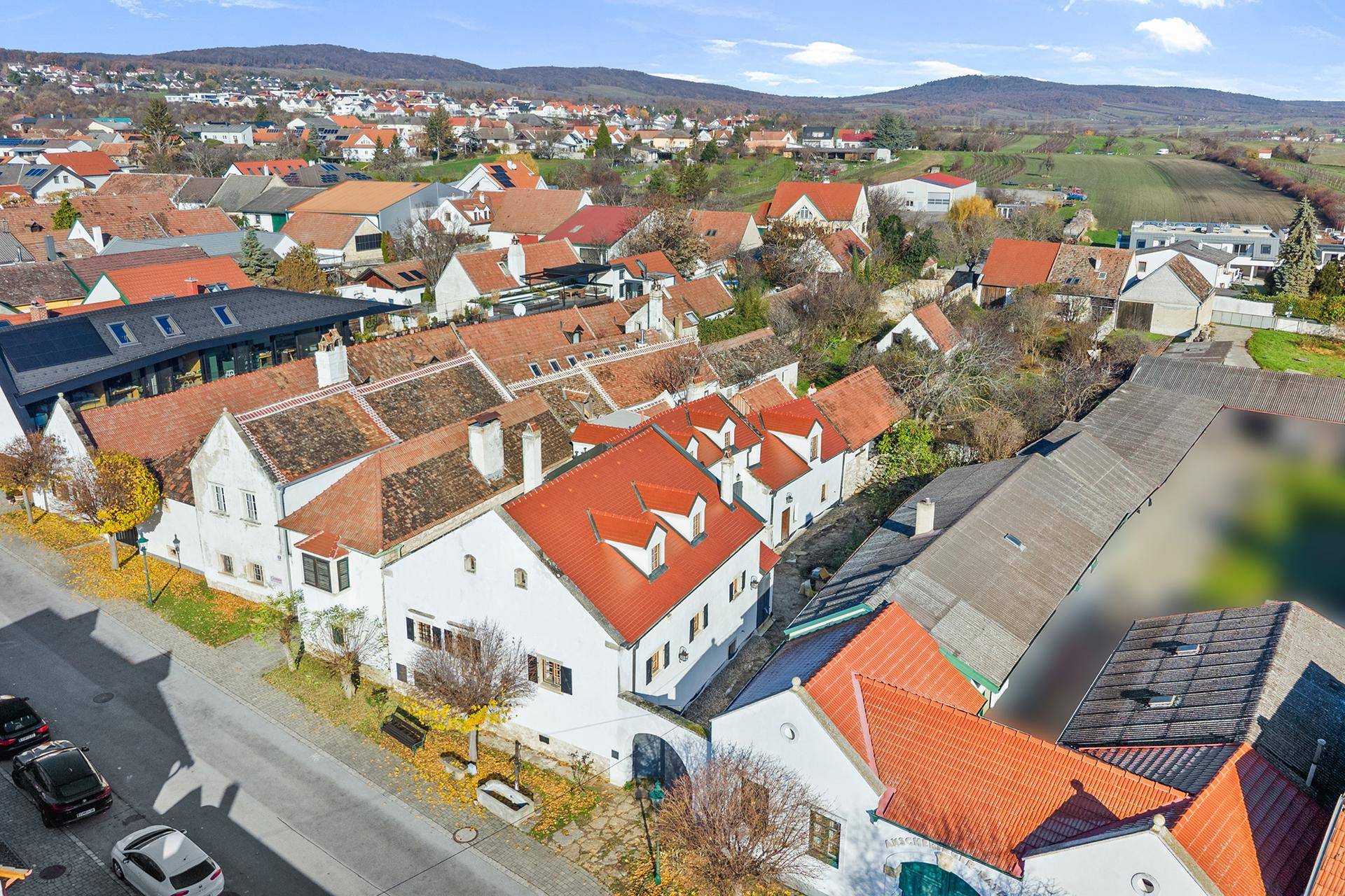 Luftaufnahme eines Dorfes mit traditionellen Häusern, roten Dächern und umliegender Landschaft.