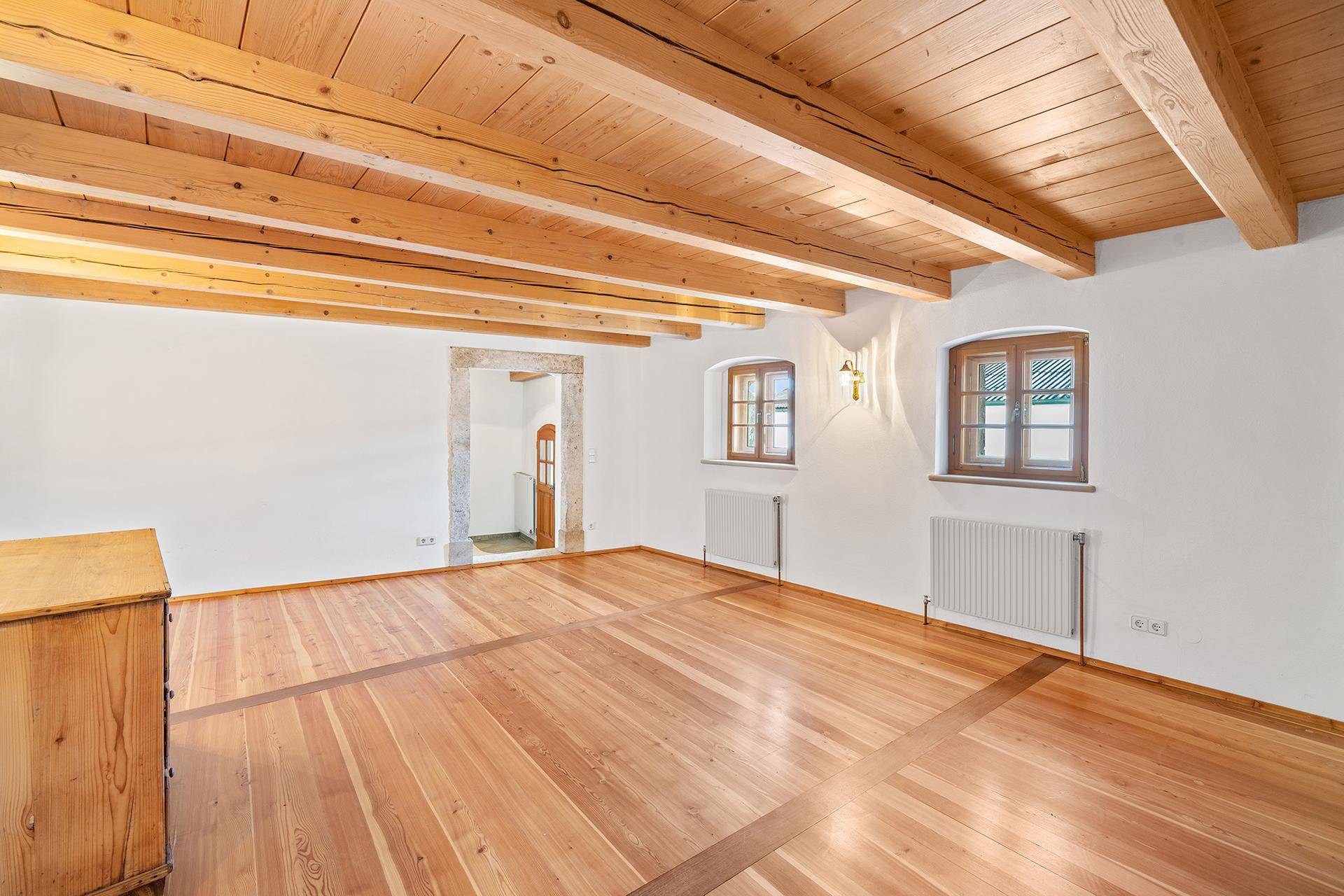 Geräumiger Wohnraum mit Holzbalkendecke, Holzboden und weißen Wänden.
