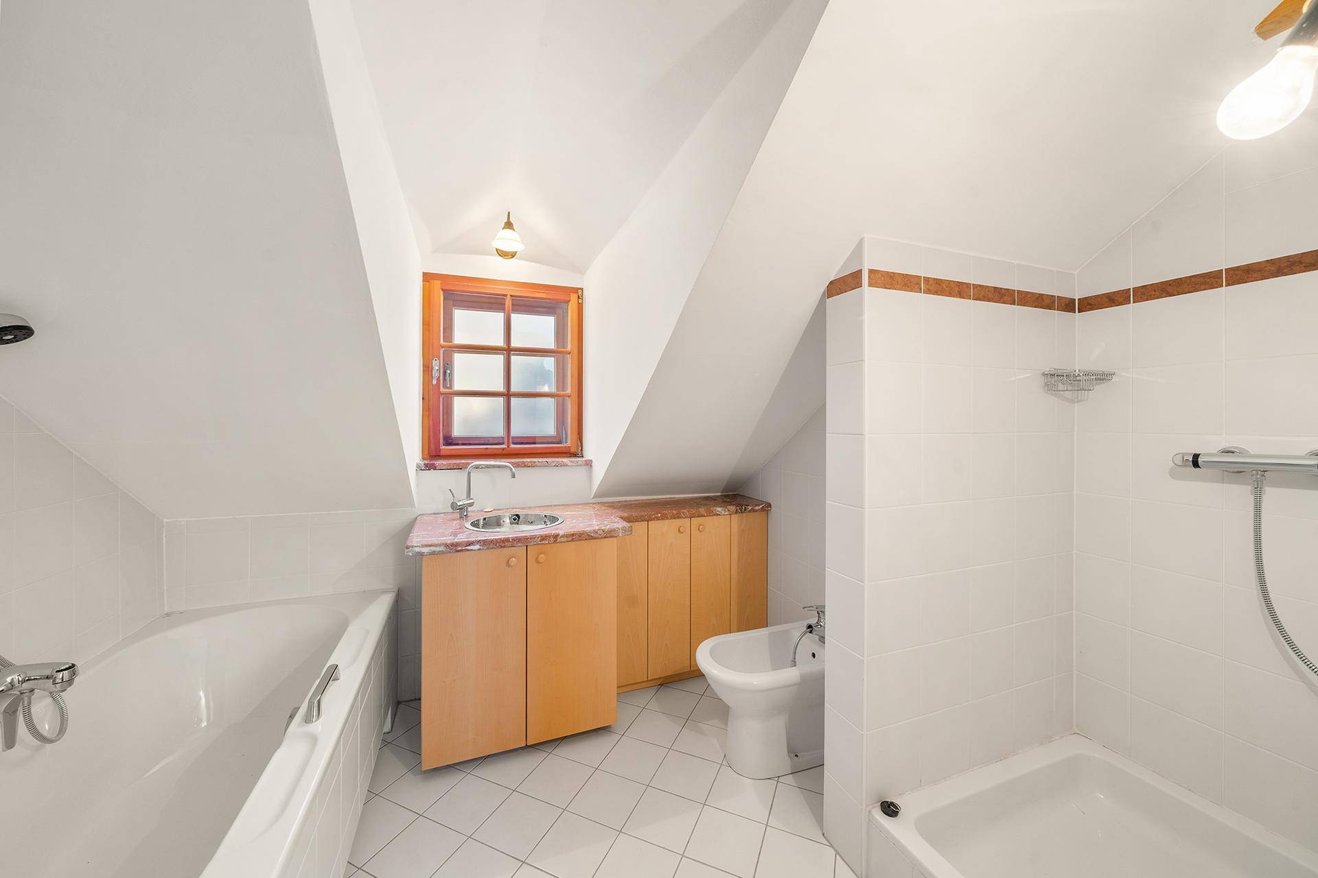 Badezimmer im Dachgeschoss mit Badewanne, Dusche, Bidet und Fenster.