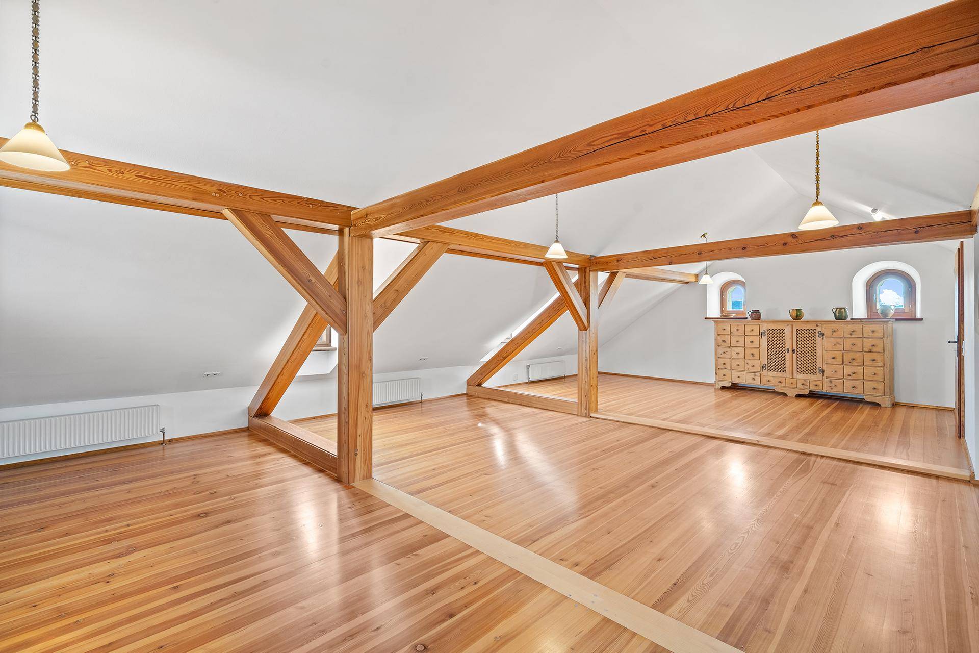 Großer offener Raum im Dachgeschoss mit sichtbaren Holzbalken und Holzboden.