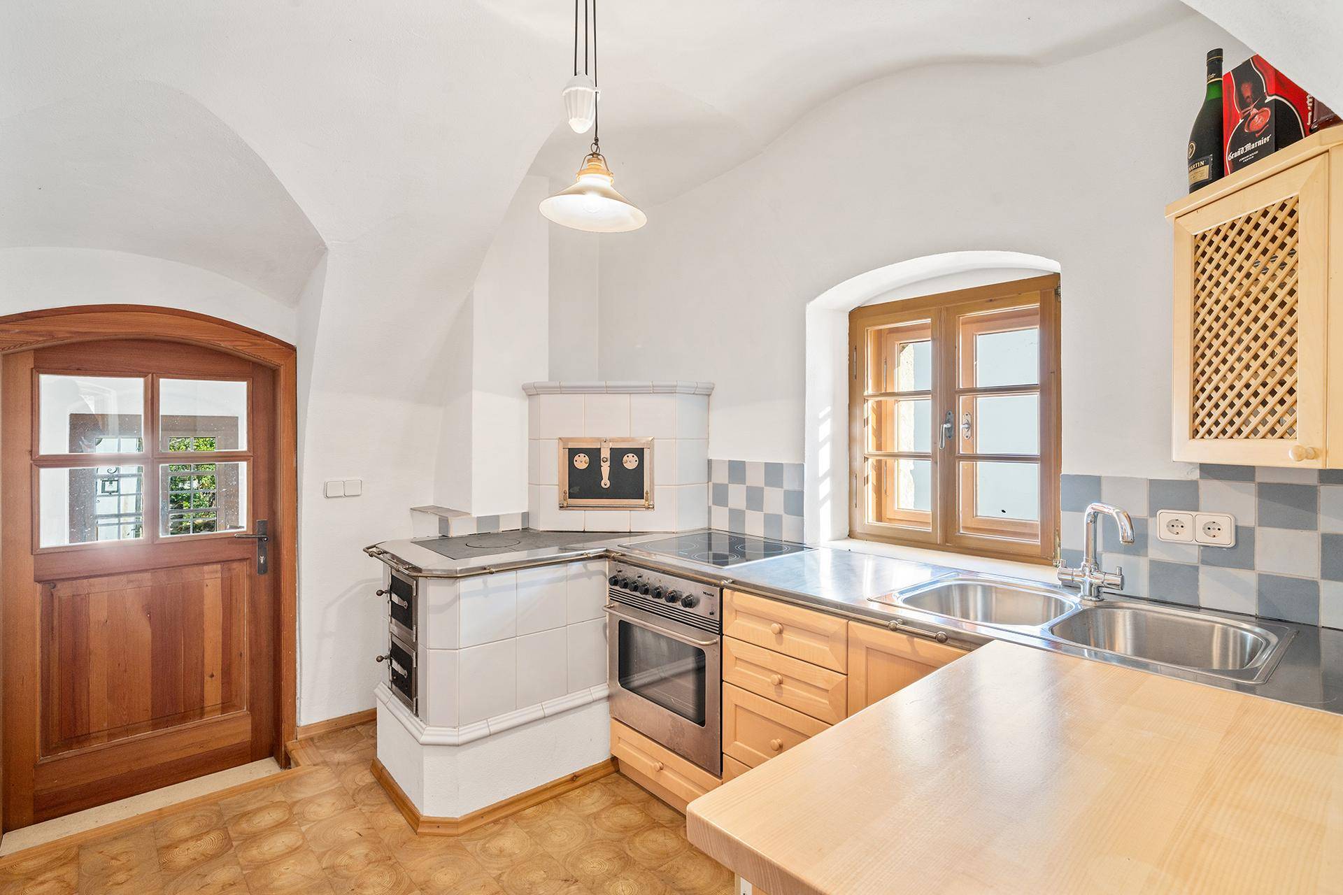 Traditionelle Küche mit Holzelementen, Kachelofen, Spülbecken und Fenster.