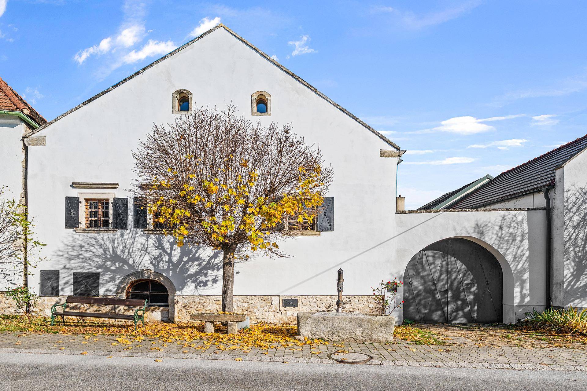 Historisches Gebäude mit weißer Fassade, Holztüren und einem Baum im Vordergrund.