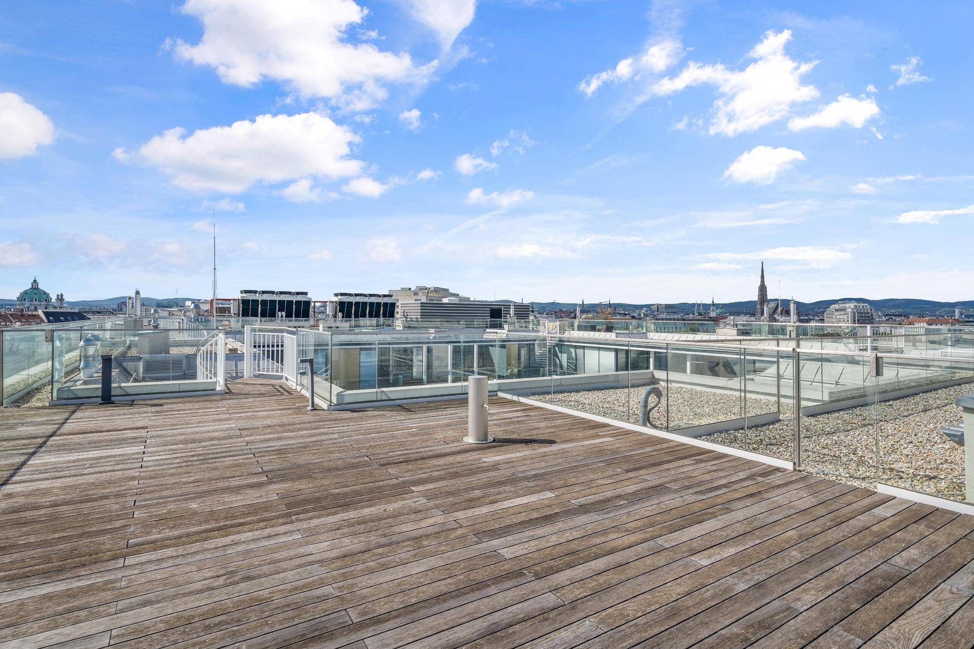 Geräumige Dachterrasse mit Holzboden, Glasgeländer und weitem Blick über die Stadt.
