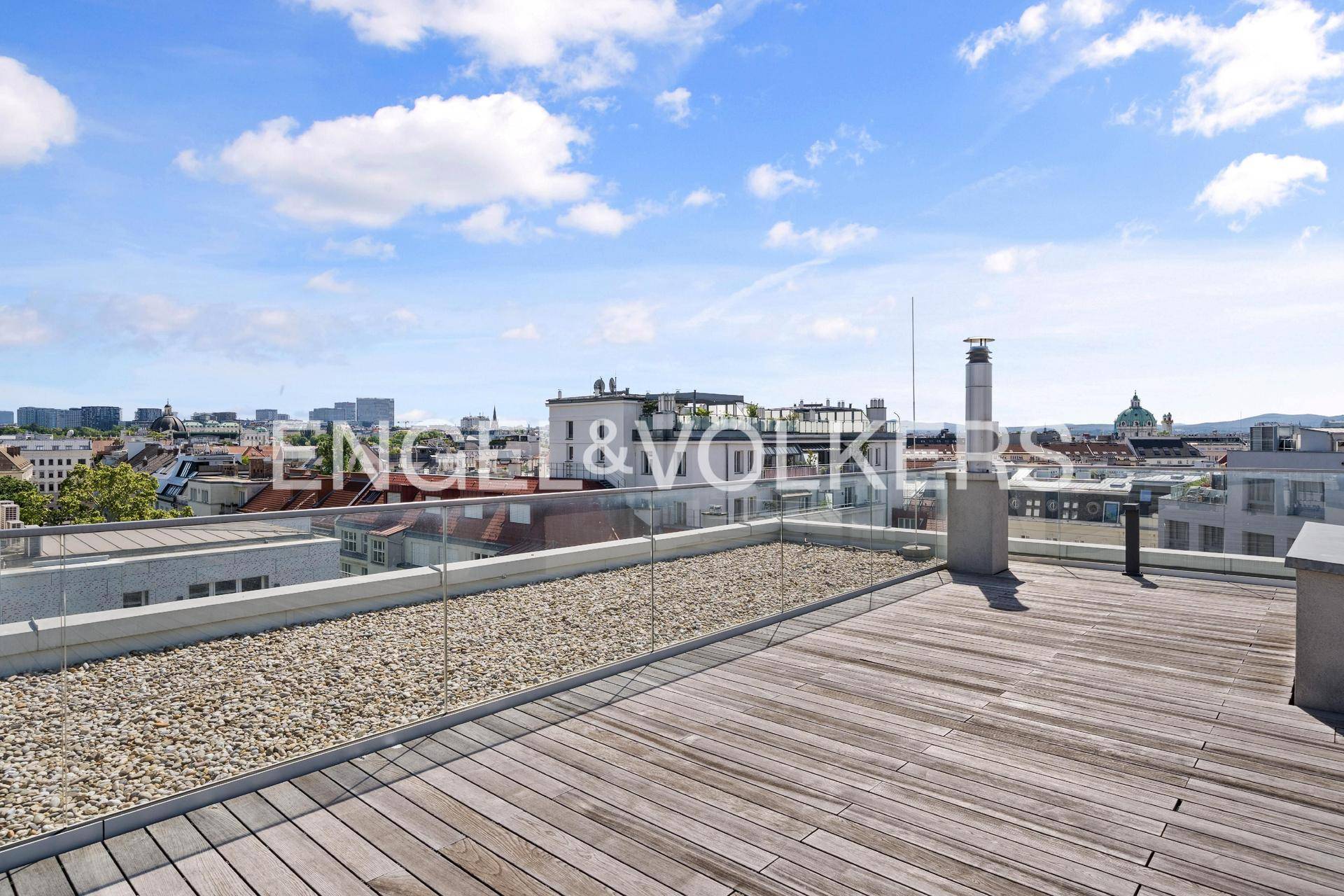 Weitläufige Dachterrasse mit Holzboden, Kiesflächen und Panoramablick über die Stadt.