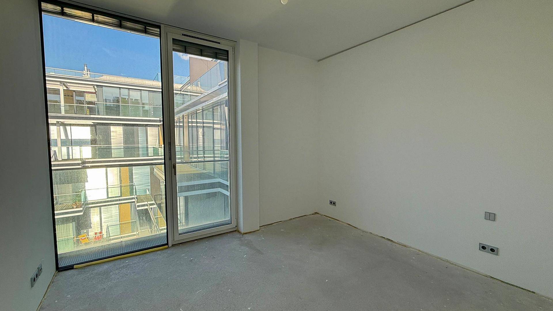 Schlafzimmer im Rohbauzustand mit Betonboden und großen Fenstern.