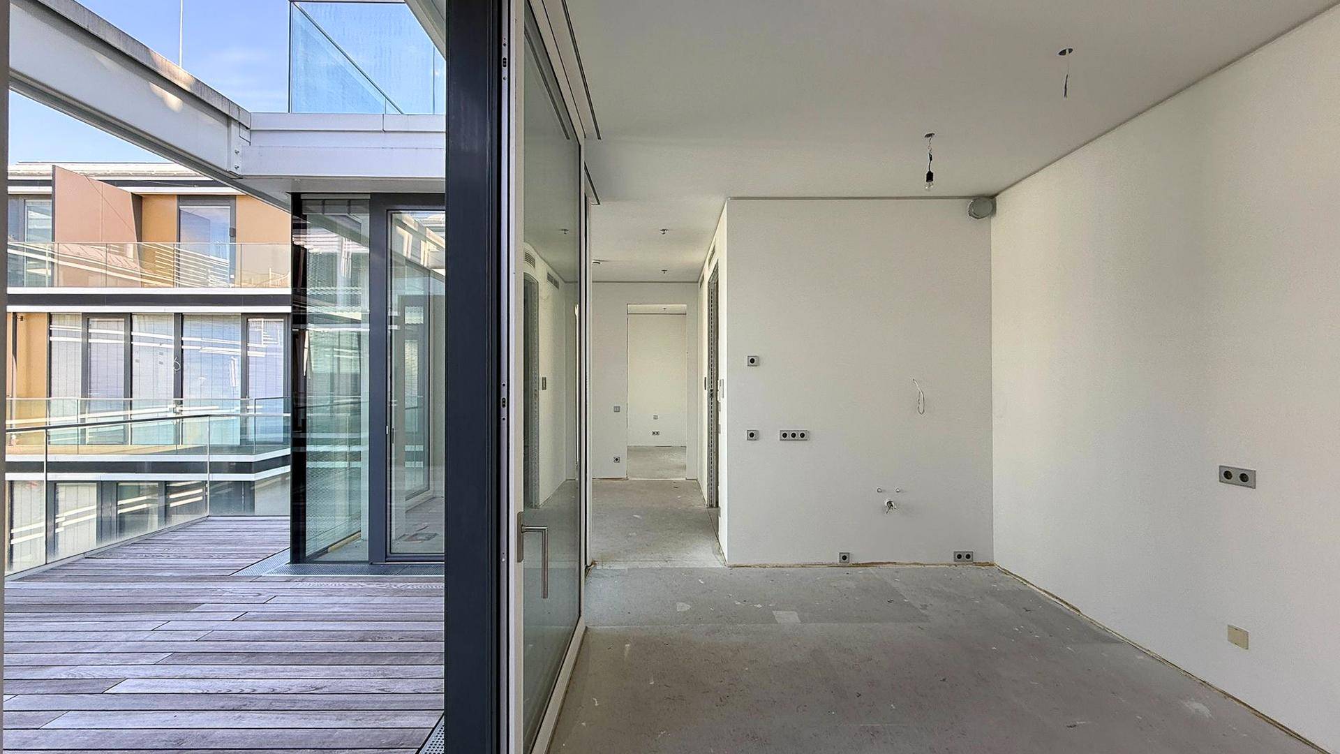 Heller Rohbau-Innenraum mit Betonboden und großen Fenstern für viel Tageslicht.
