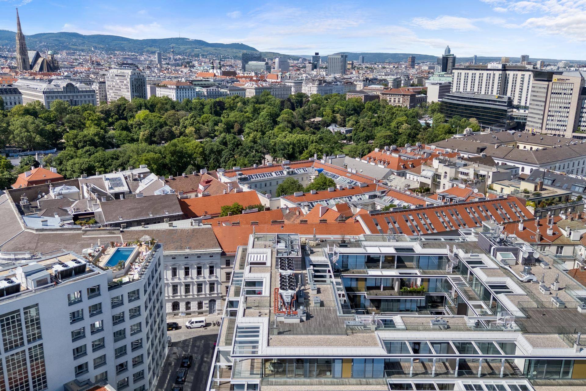 Panoramablick über eine Stadt mit vielen Gebäuden, Grünflächen und Bergen im Hintergrund.