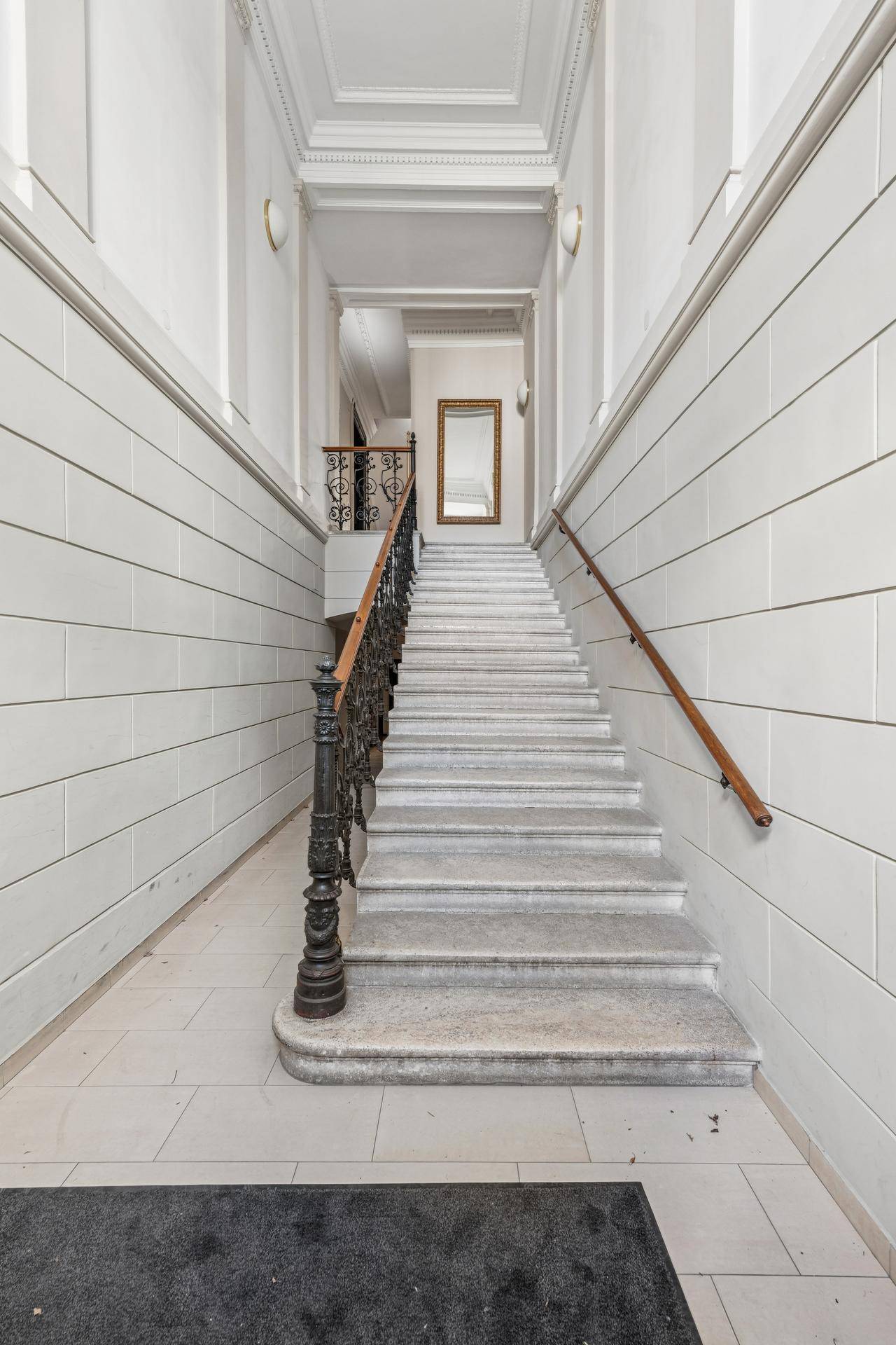 Elegantes Treppenhaus mit Steinstufen, schmiedeeisernem Geländer und hohem Spiegel.