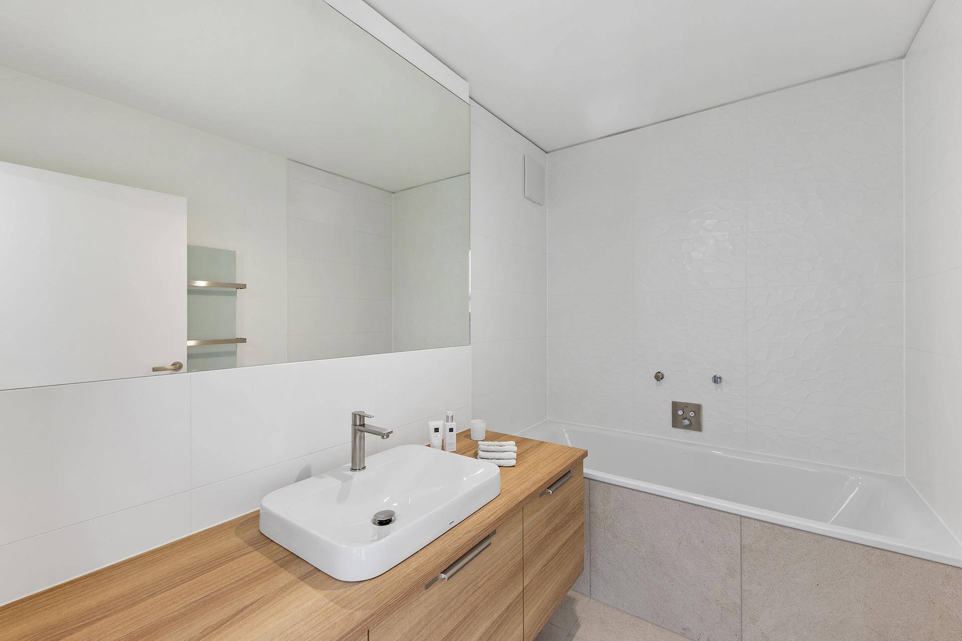 Modernes Badezimmer mit Badewanne, Holzwaschtisch und großem Spiegel.
