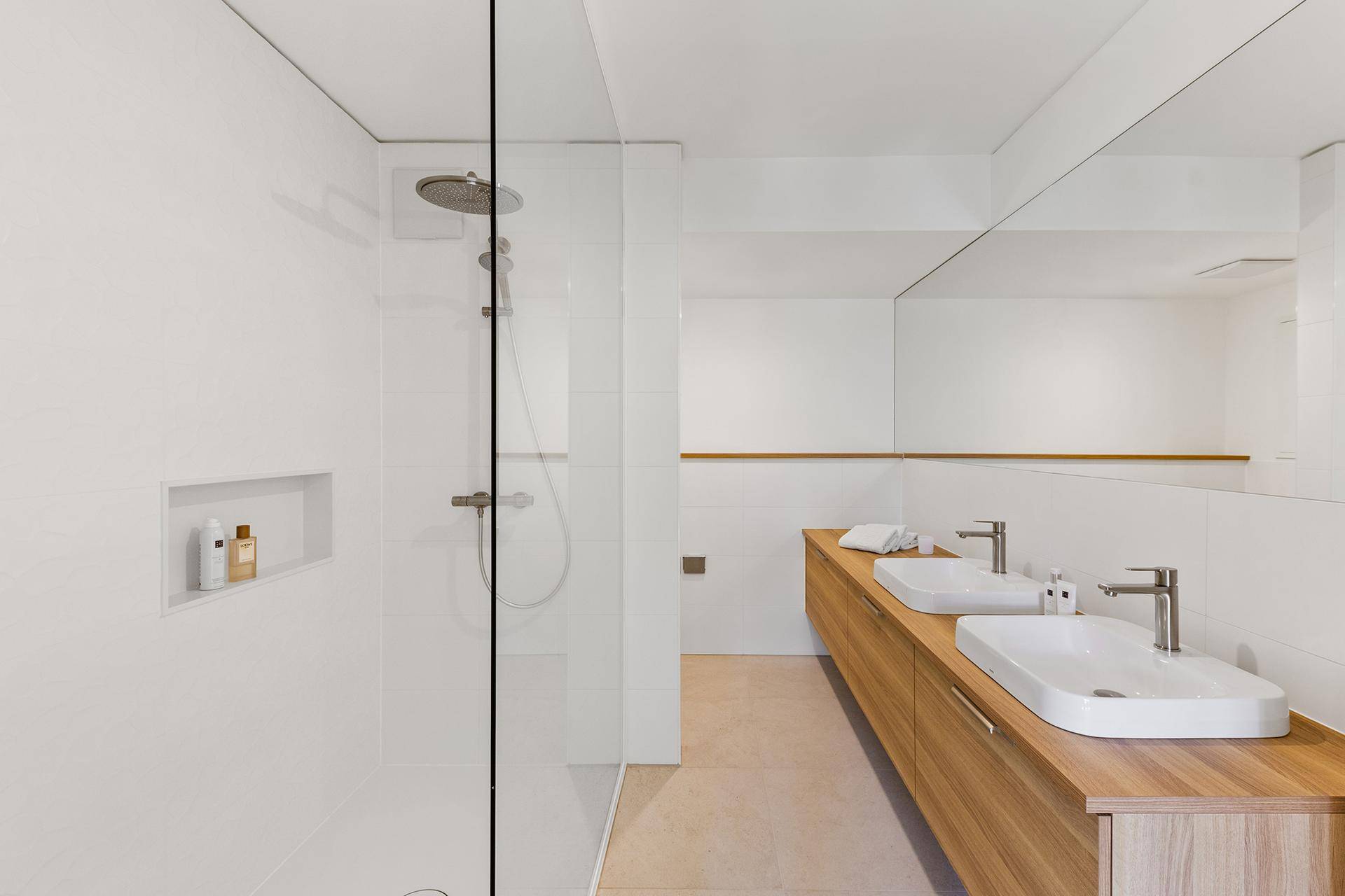 Elegantes Badezimmer mit begehbarer Dusche, Regendusche und Doppelwaschbecken auf Holzunterschrank.