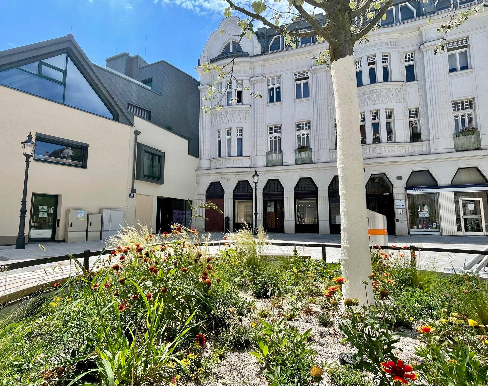 Grüne Oase in der Stadt mit Blumenbeeten und historischen Gebäuden im Hintergrund.