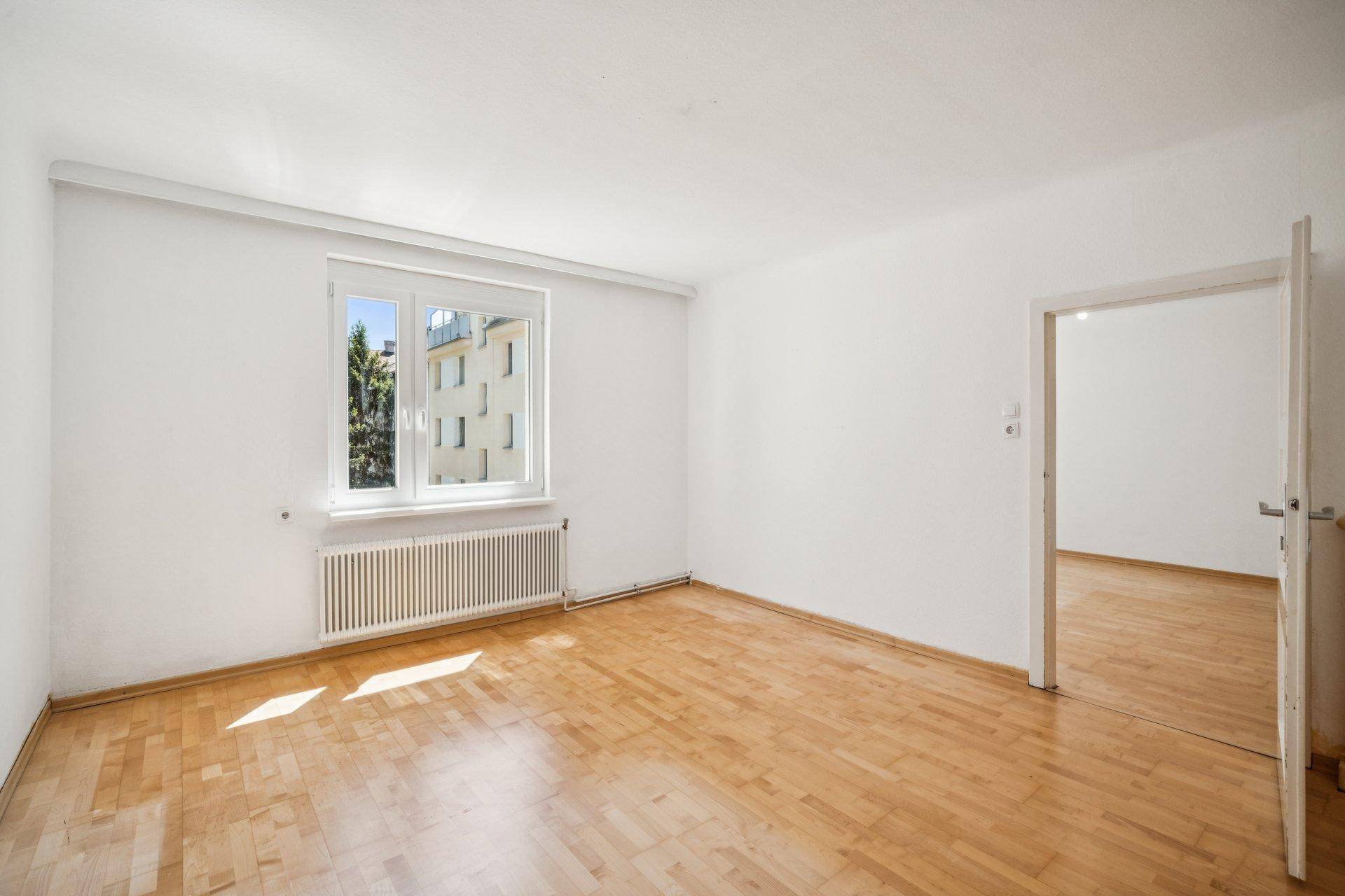 Helles, unmöbliertes Zimmer mit Parkettboden und Blick auf die umliegenden Gebäude.