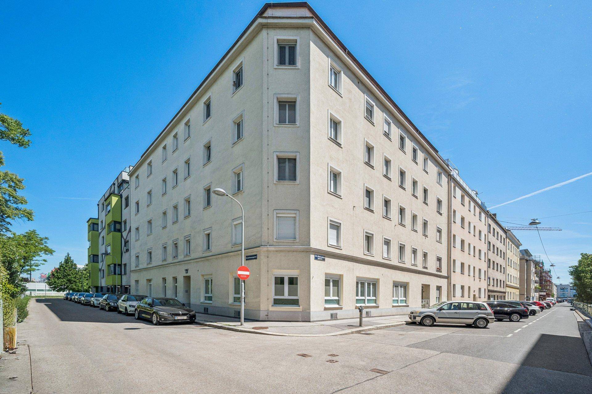 Eckgebäude in städtischer Umgebung mit vielen Fenstern und Parkplätzen an der Straße.