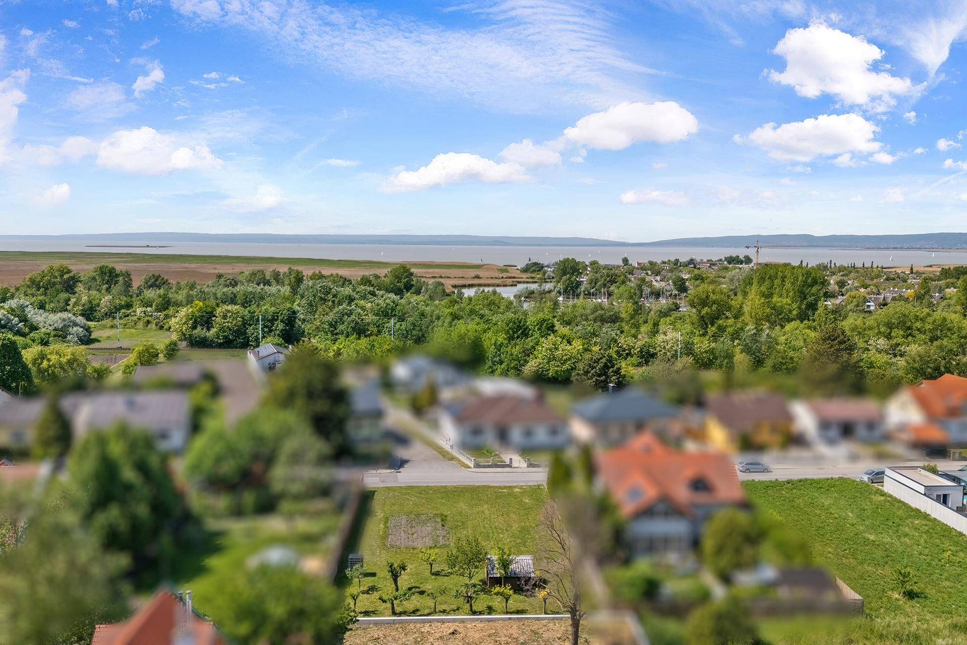 Weitläufige Luftaufnahme einer Wohngegend mit viel Grün und einem See am Horizont.