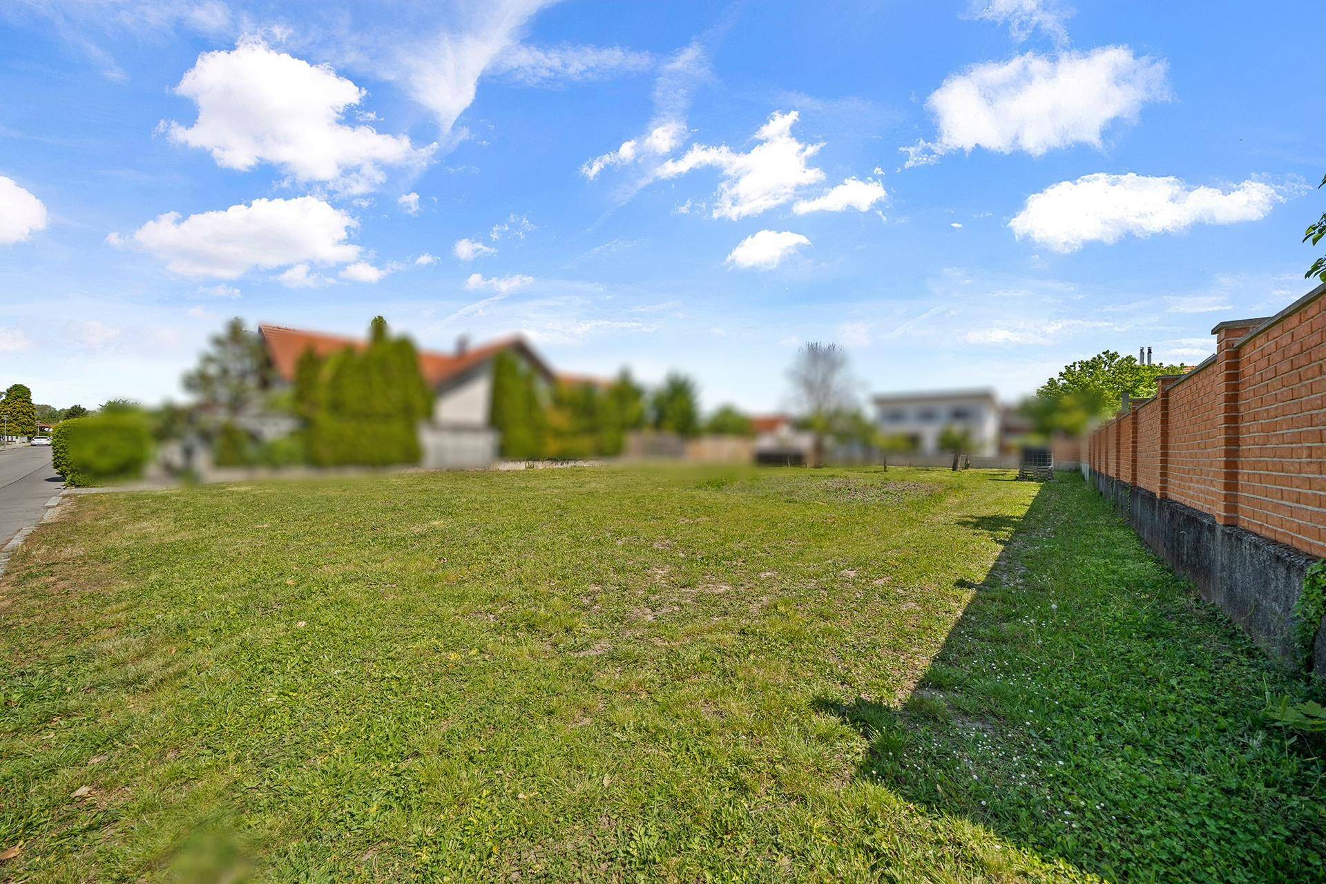 Weitläufiges, unbebautes Grundstück mit Rasenfläche und einer Ziegelmauer im Hintergrund.