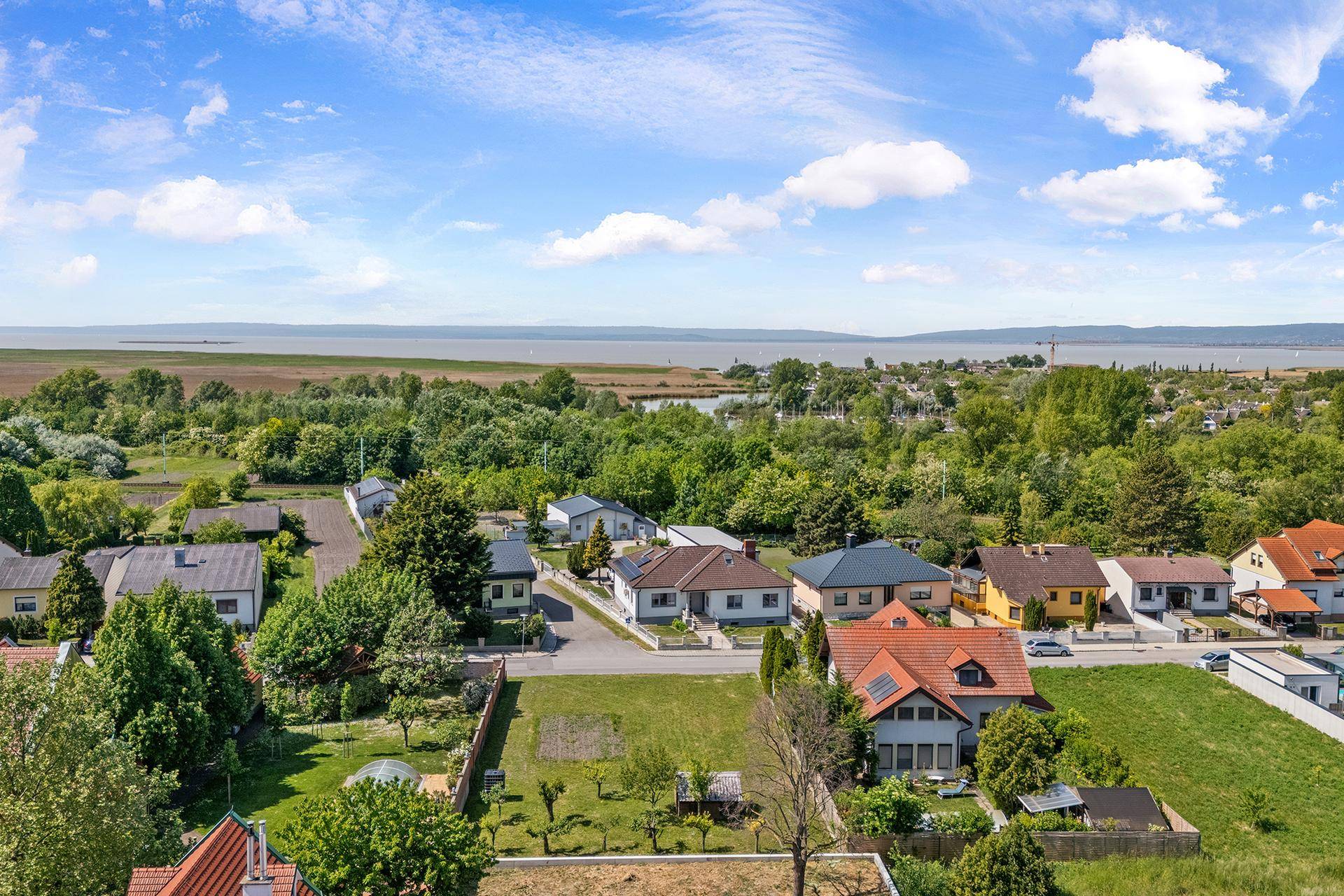 Weitläufige Luftaufnahme einer Wohngegend mit viel Grün und einem See am Horizont.
